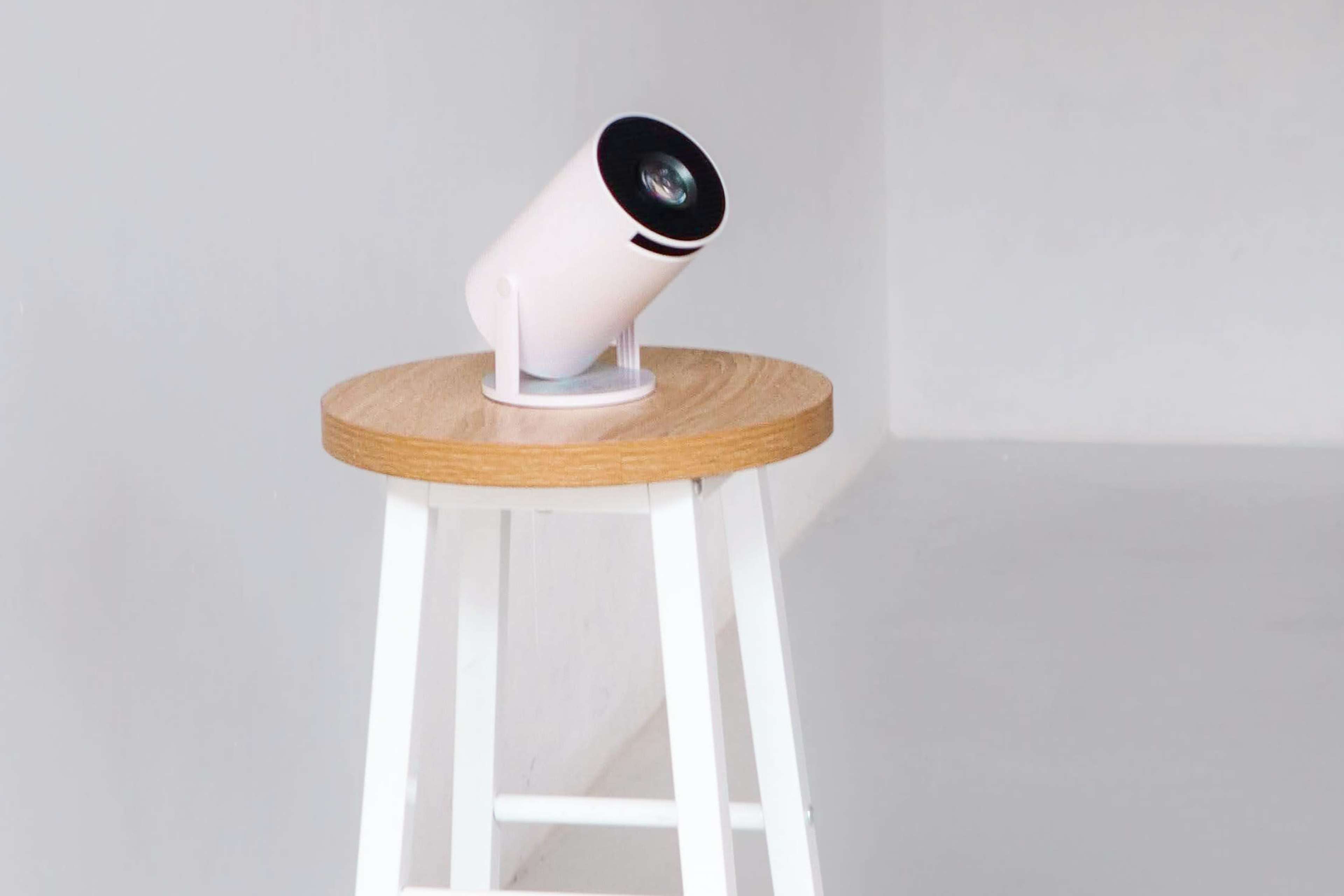 A cylindrical projector sits atop a wooden stool in a minimalist room.