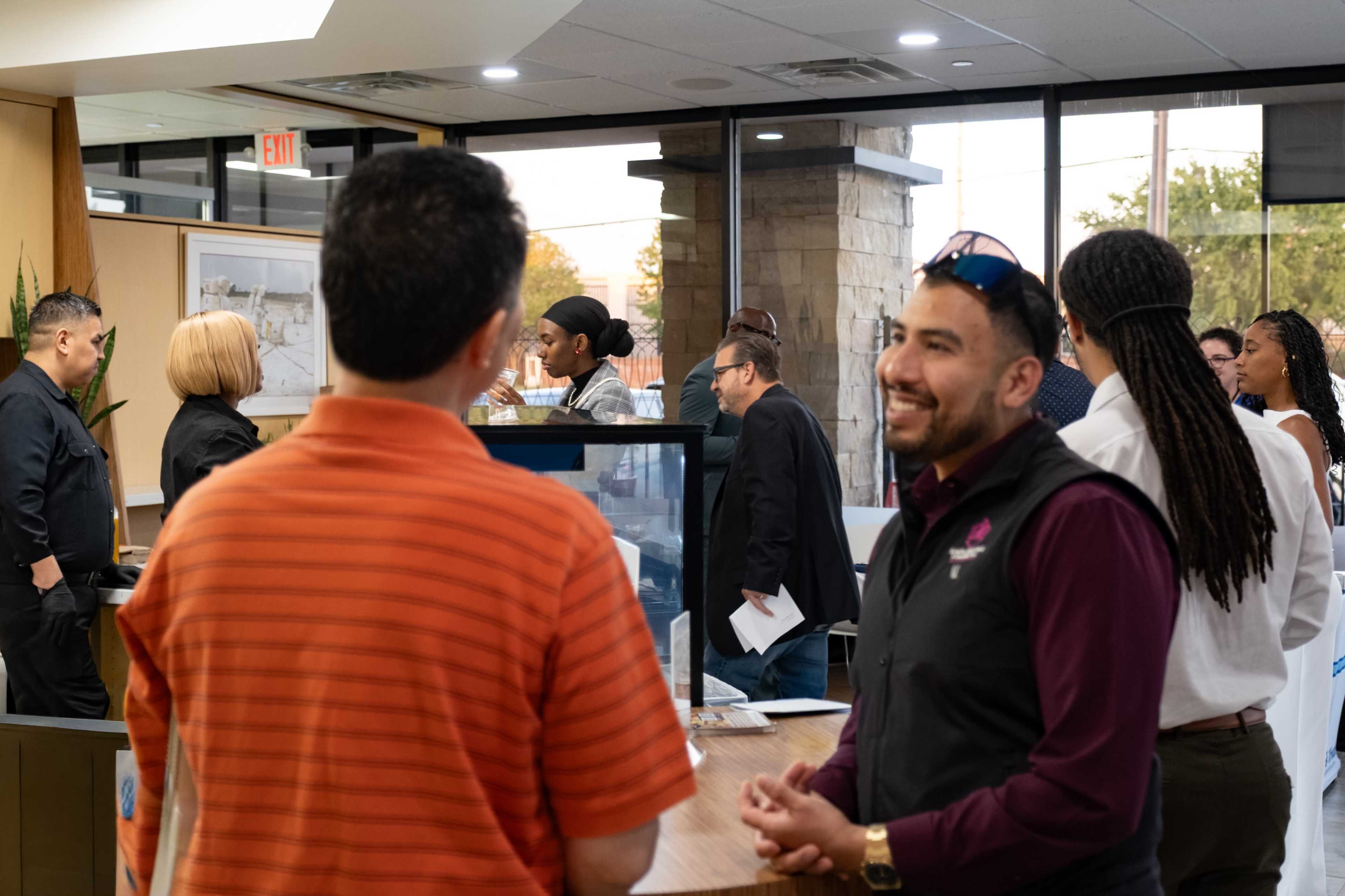 A group of people is engaged in conversation in a modern office setting with a reception area visible in the background.