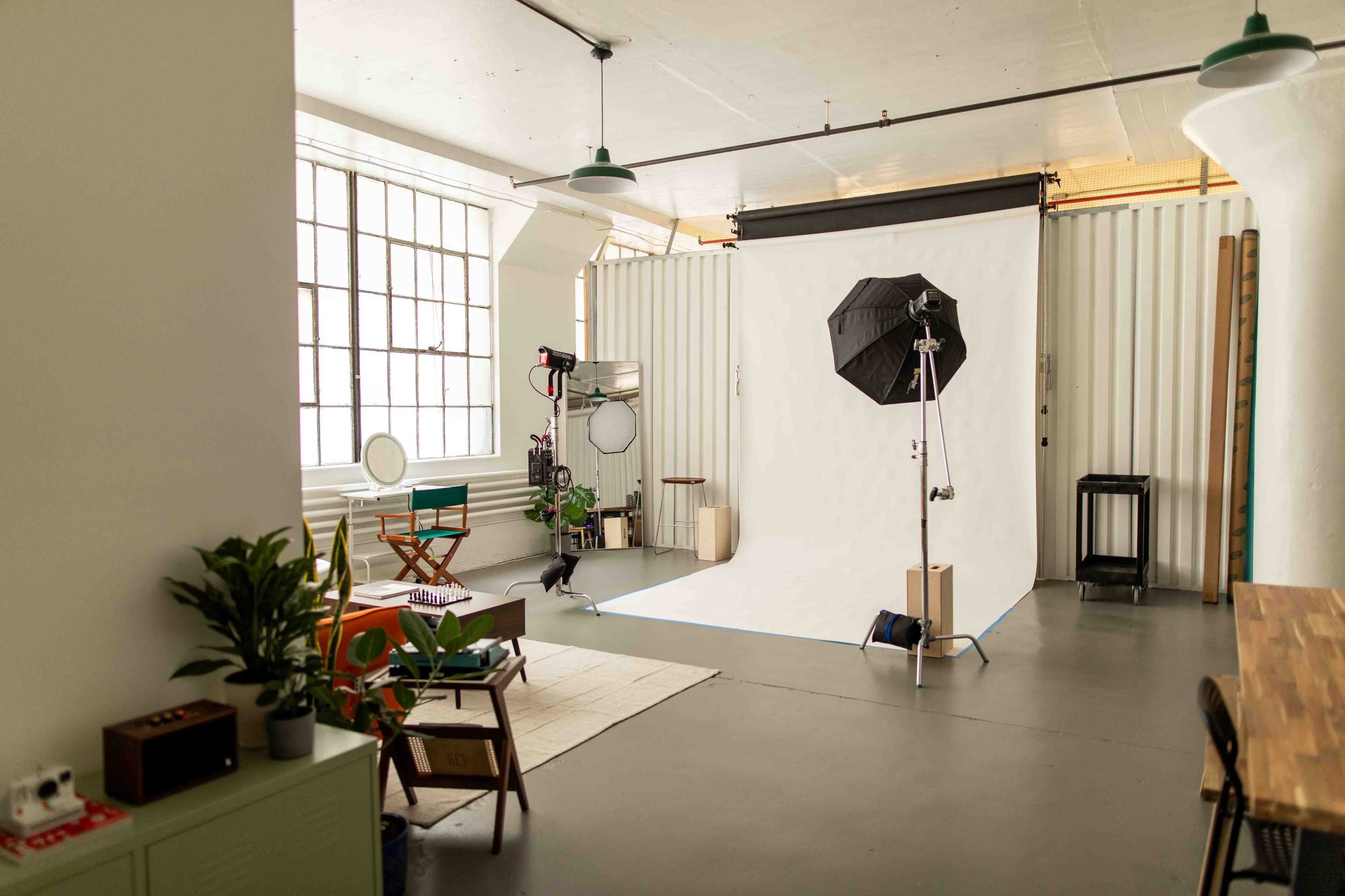A well-lit photography studio with a seamless white backdrop, lighting equipment, and a few pieces of furniture.