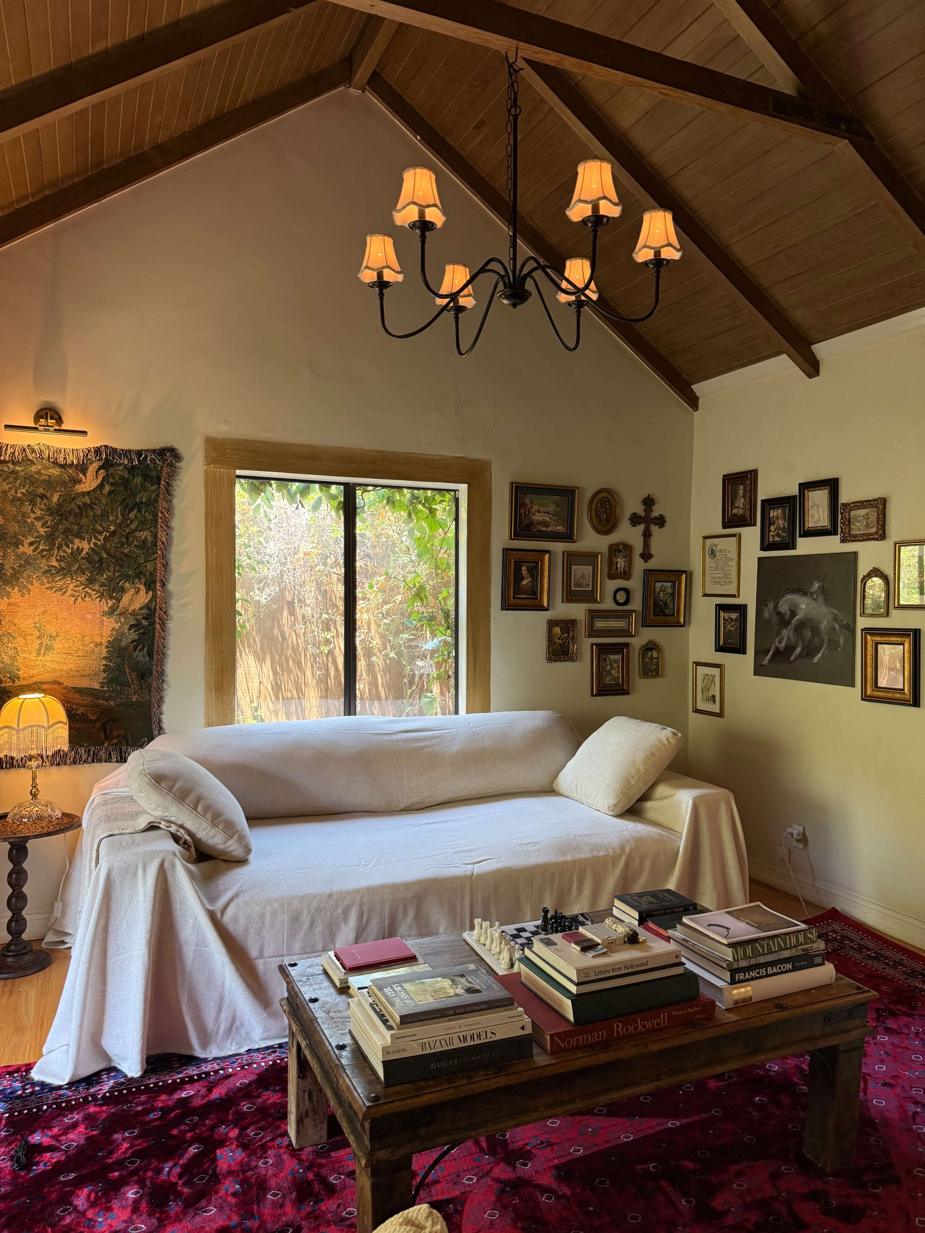 The image shows a cozy living room with a white couch, a wooden coffee table stacked with books, and a collection of framed artworks on the walls.