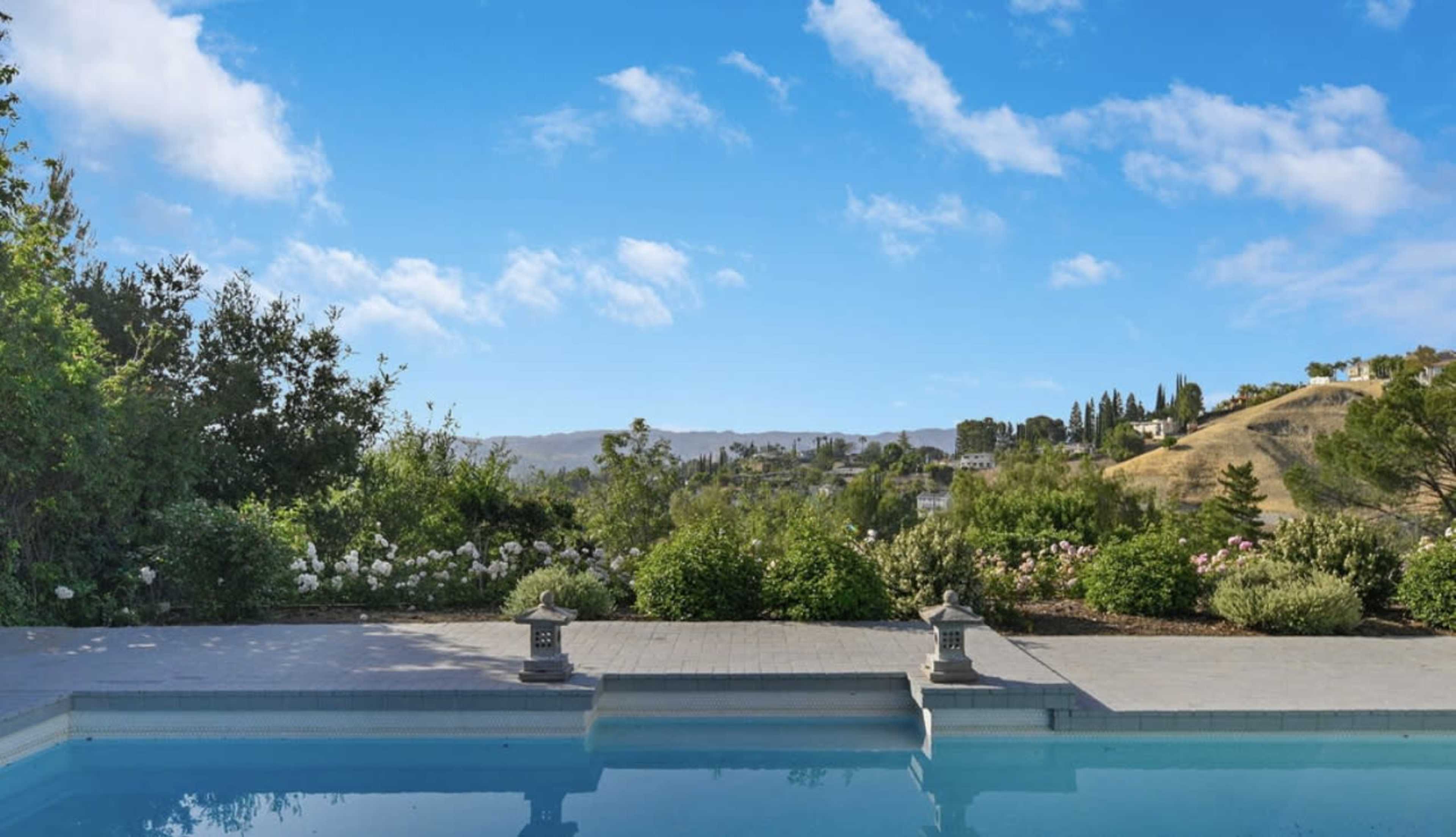 A swimming pool overlooking a landscaped garden and rolling hills under a clear blue sky.
