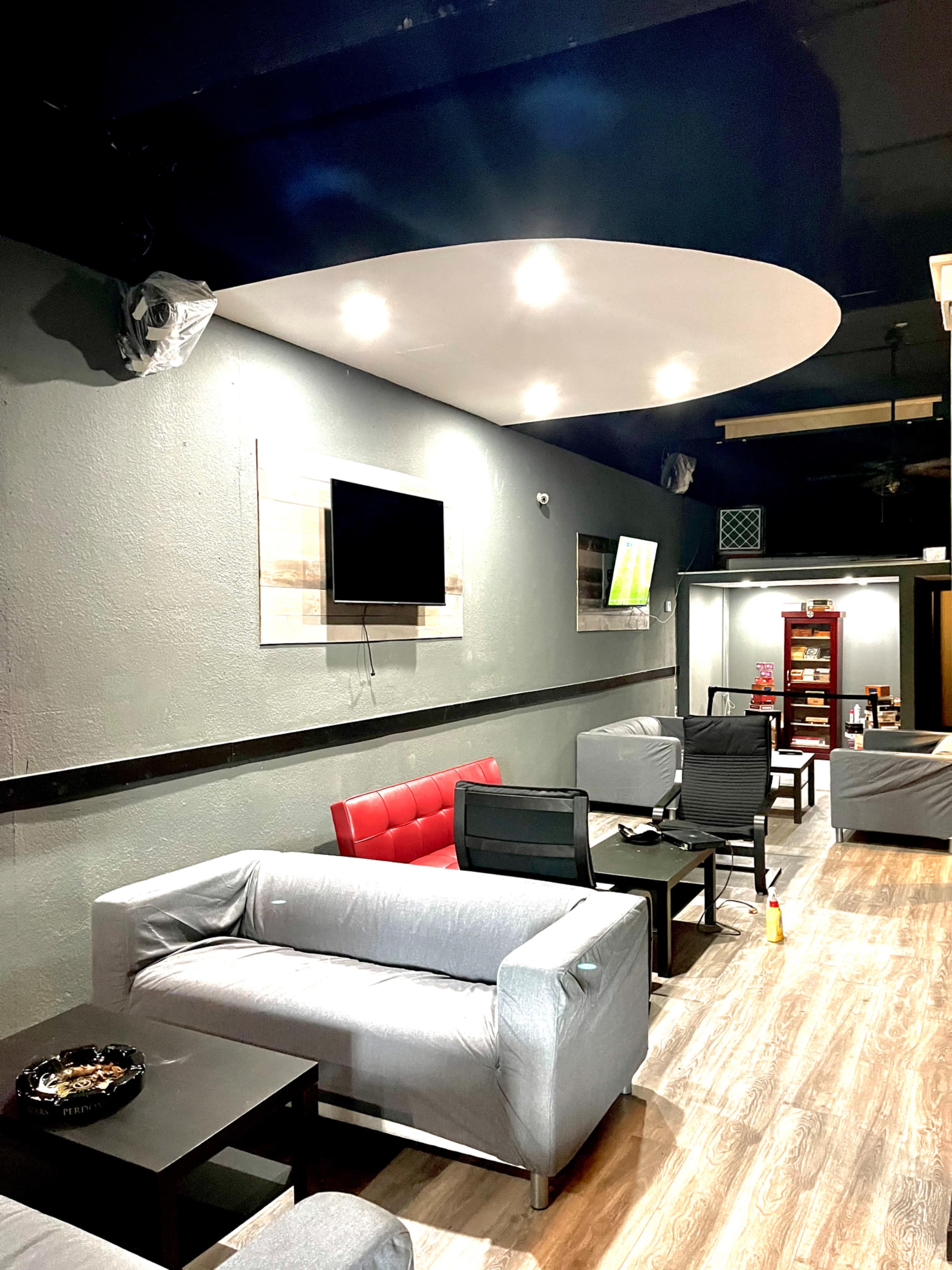 The image shows a modern lounge area with gray walls, a flat-screen TV on the wall, red and black seating, and wooden floors.