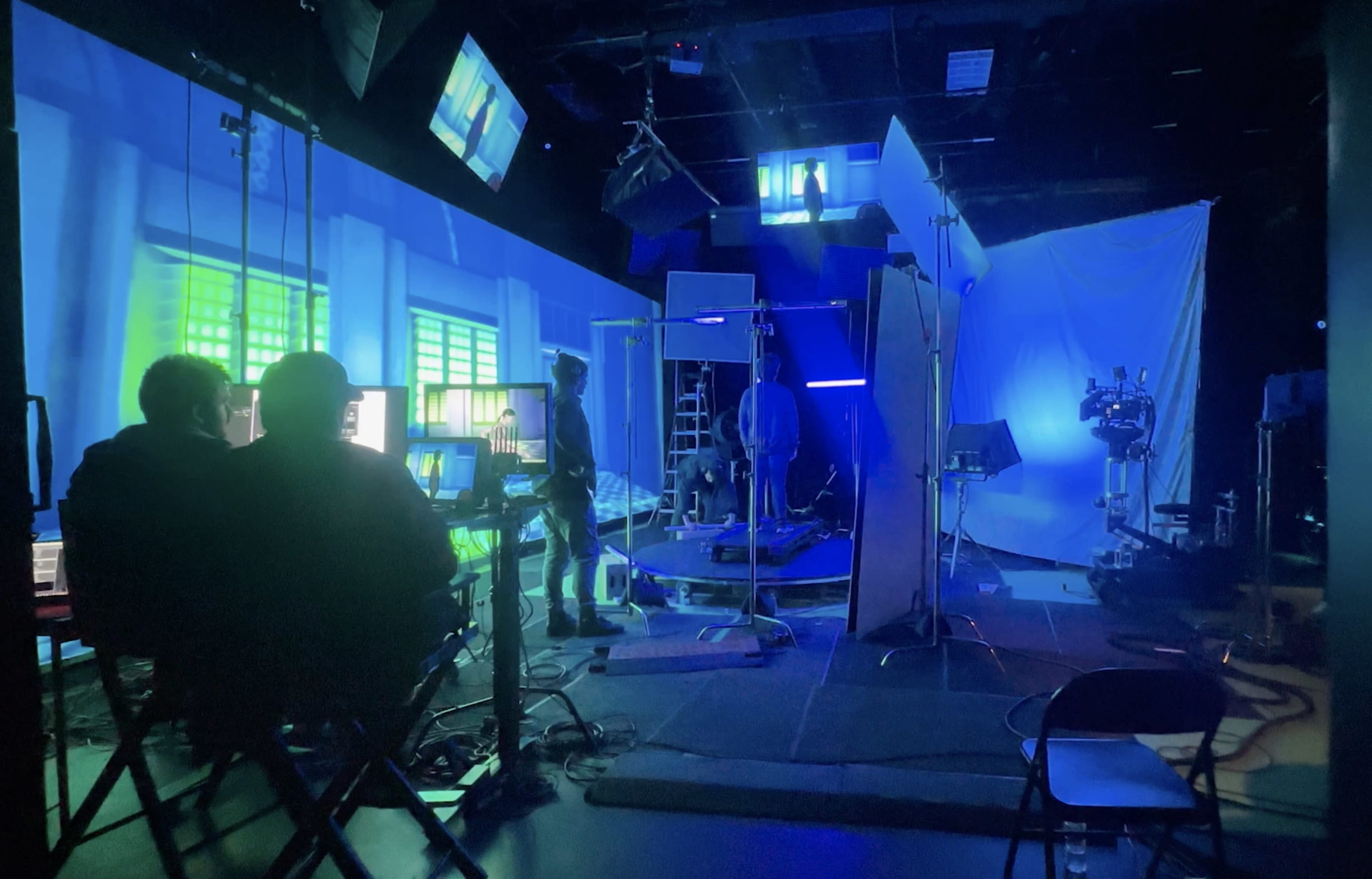 A film production studio with blue lighting, various equipment, and crew members preparing for a shoot.