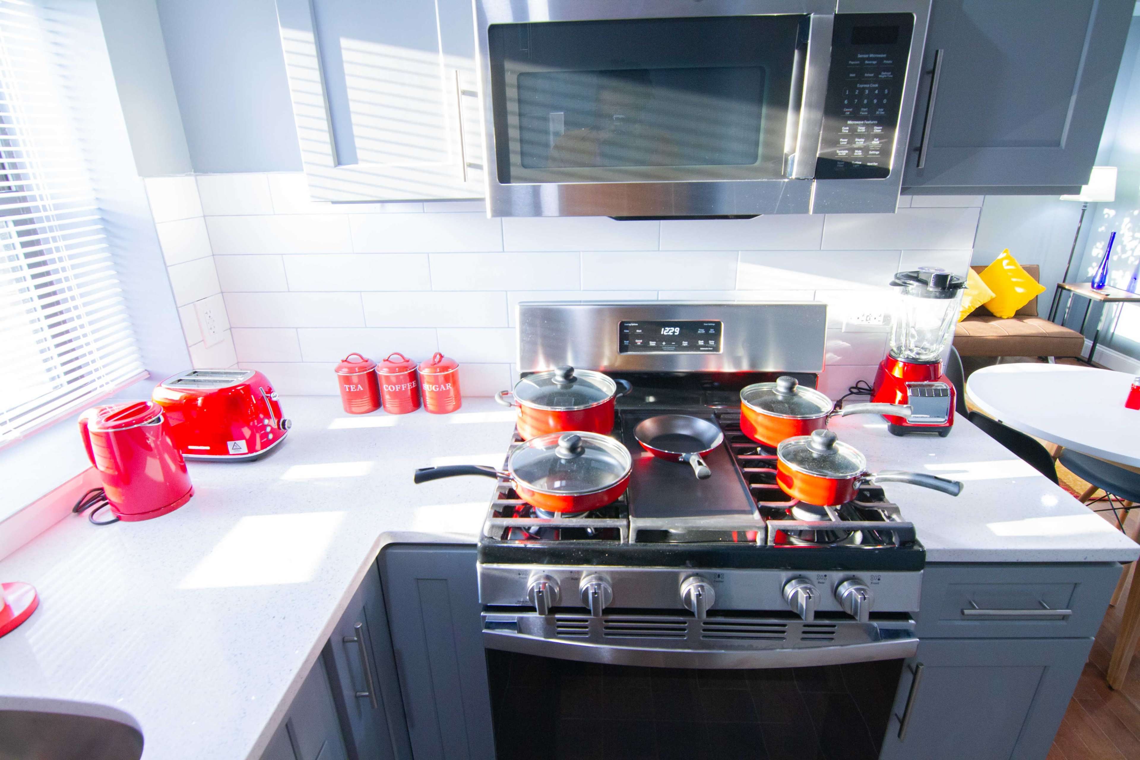 A modern kitchen countertop with a gas stove, multiple pots on the burner, a microwave above, and red kitchen appliances arranged neatly.
