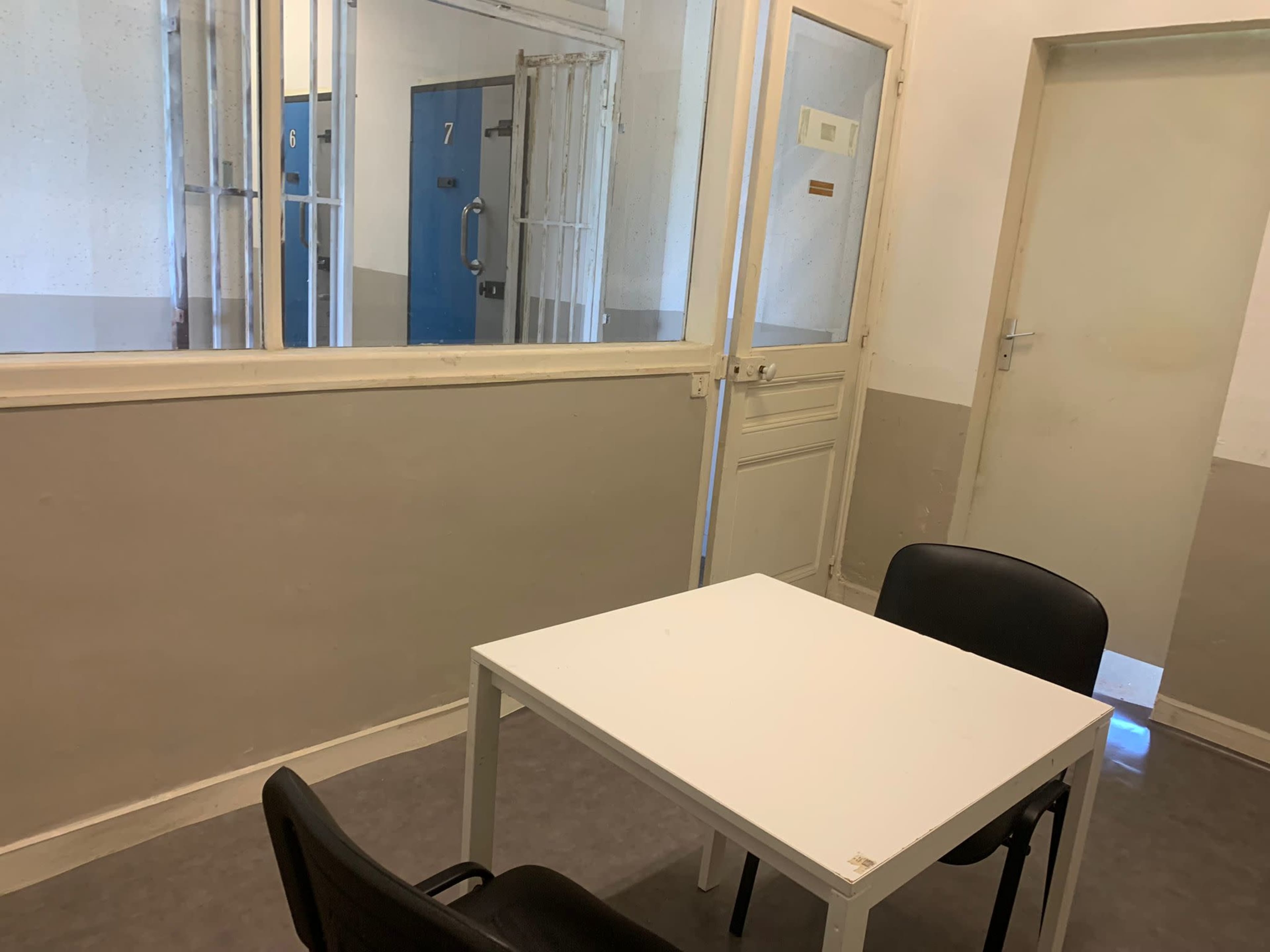 A small room with a white table and two black chairs, featuring a door and a window that look into an adjacent area.