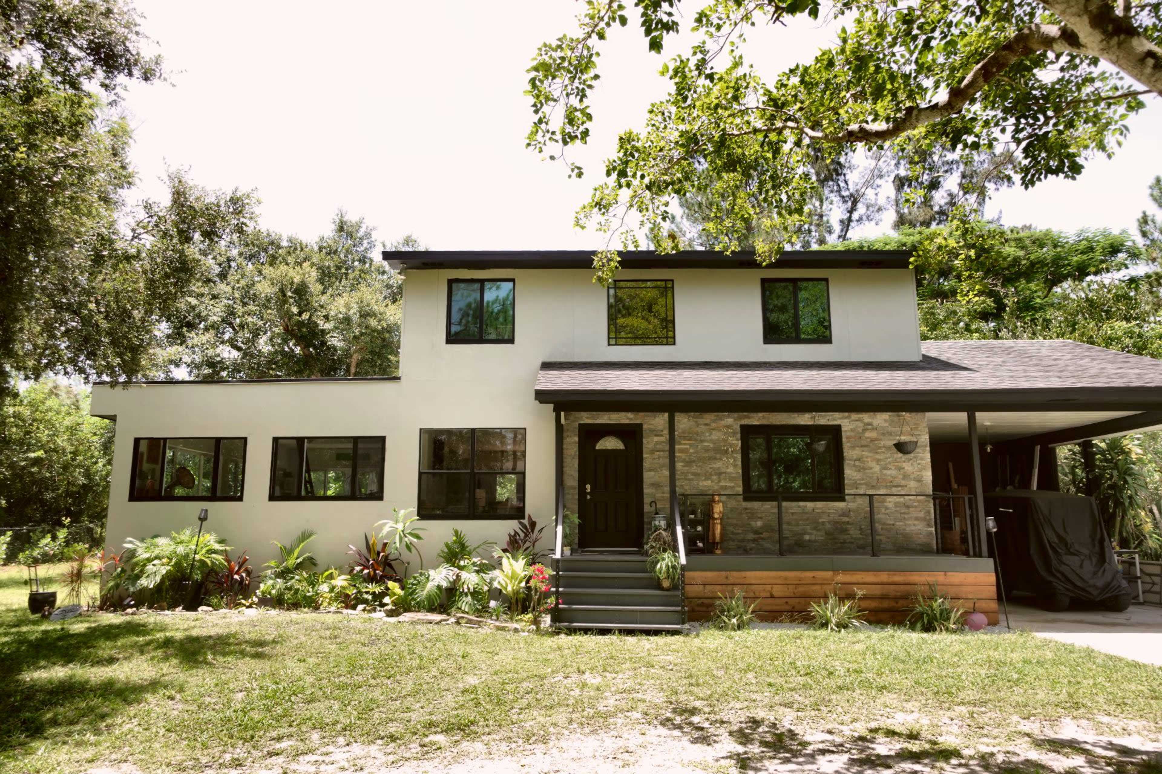 The image shows a two-story house with a stone-accented front, surrounded by greenery and landscaped flowers.