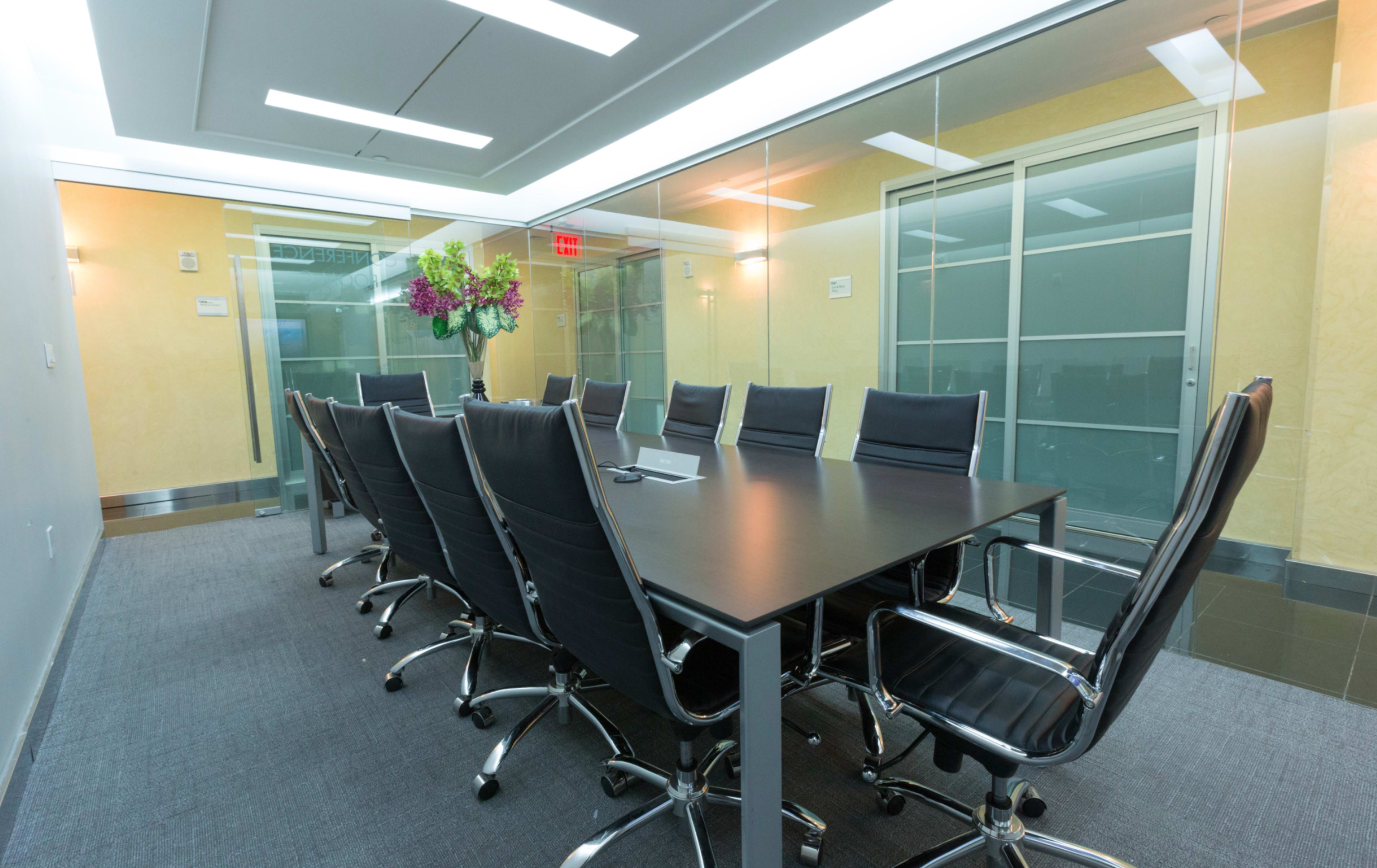 The image shows a modern conference room with a long black table surrounded by ergonomic chairs and glass walls.
