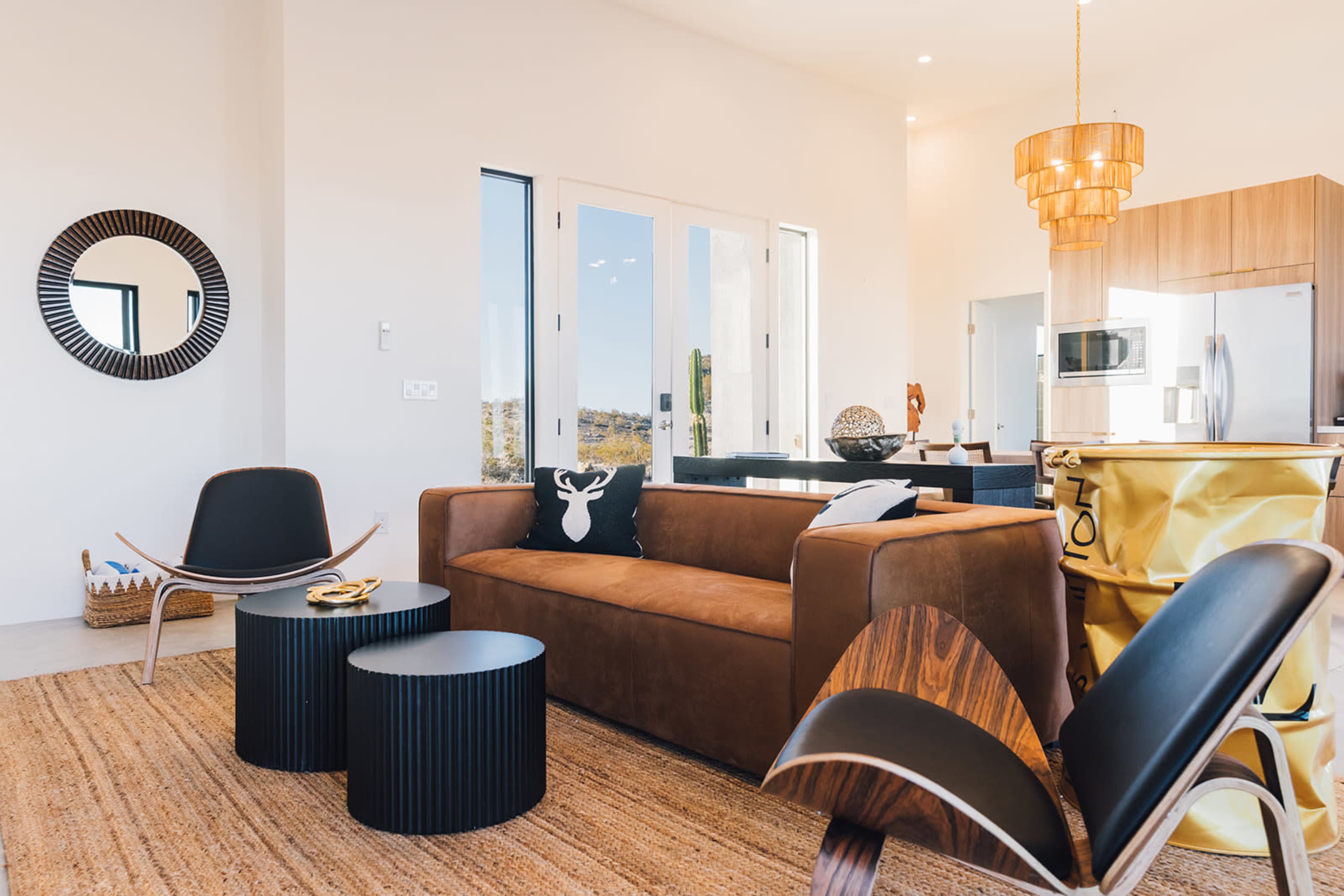 A modern living space featuring a brown leather sofa, black side tables, and contemporary chairs with a large window allowing natural light to enter.