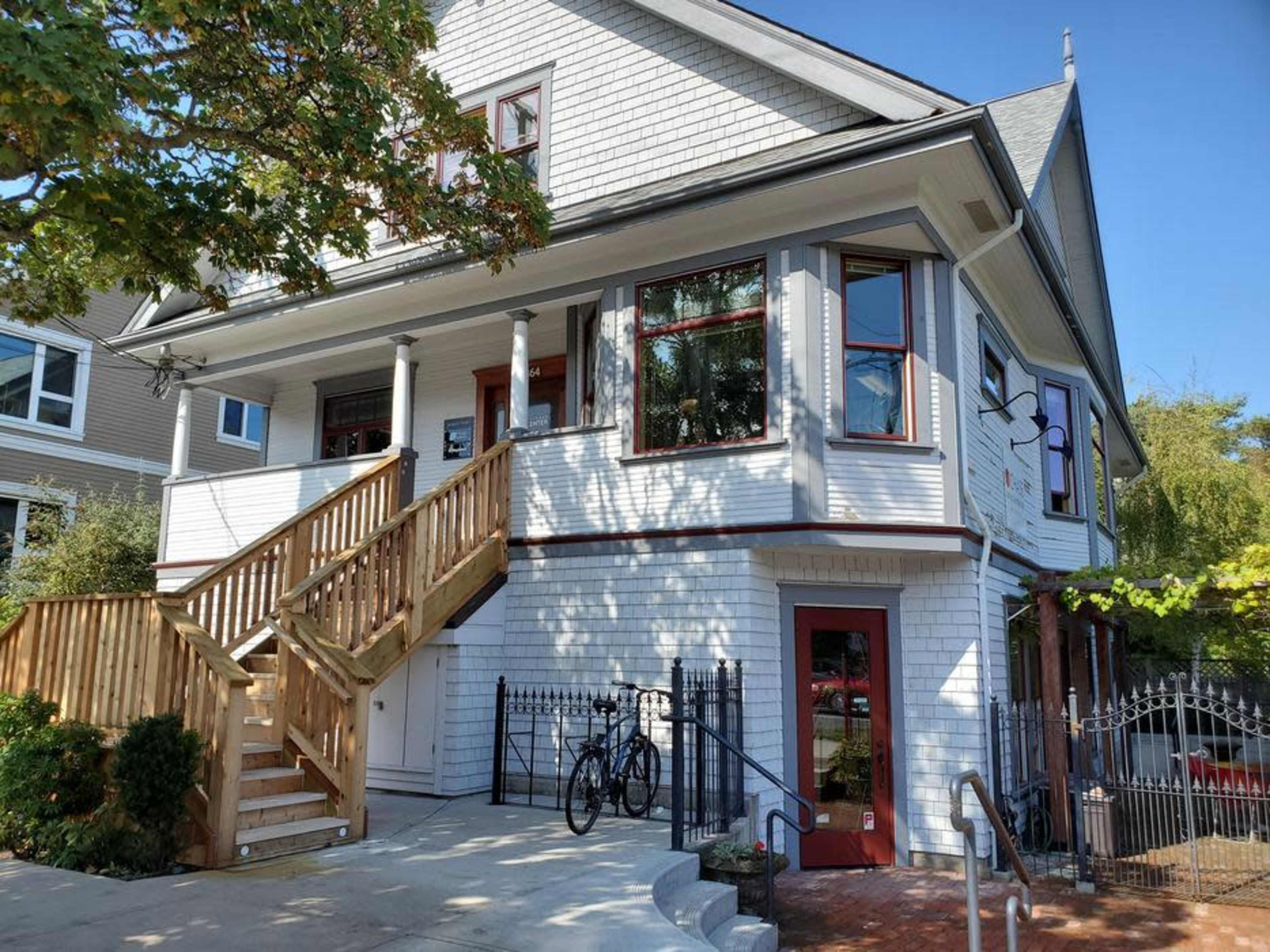 A two-story white house with a wooden staircase leading to the entrance and two bicycles parked near the door.