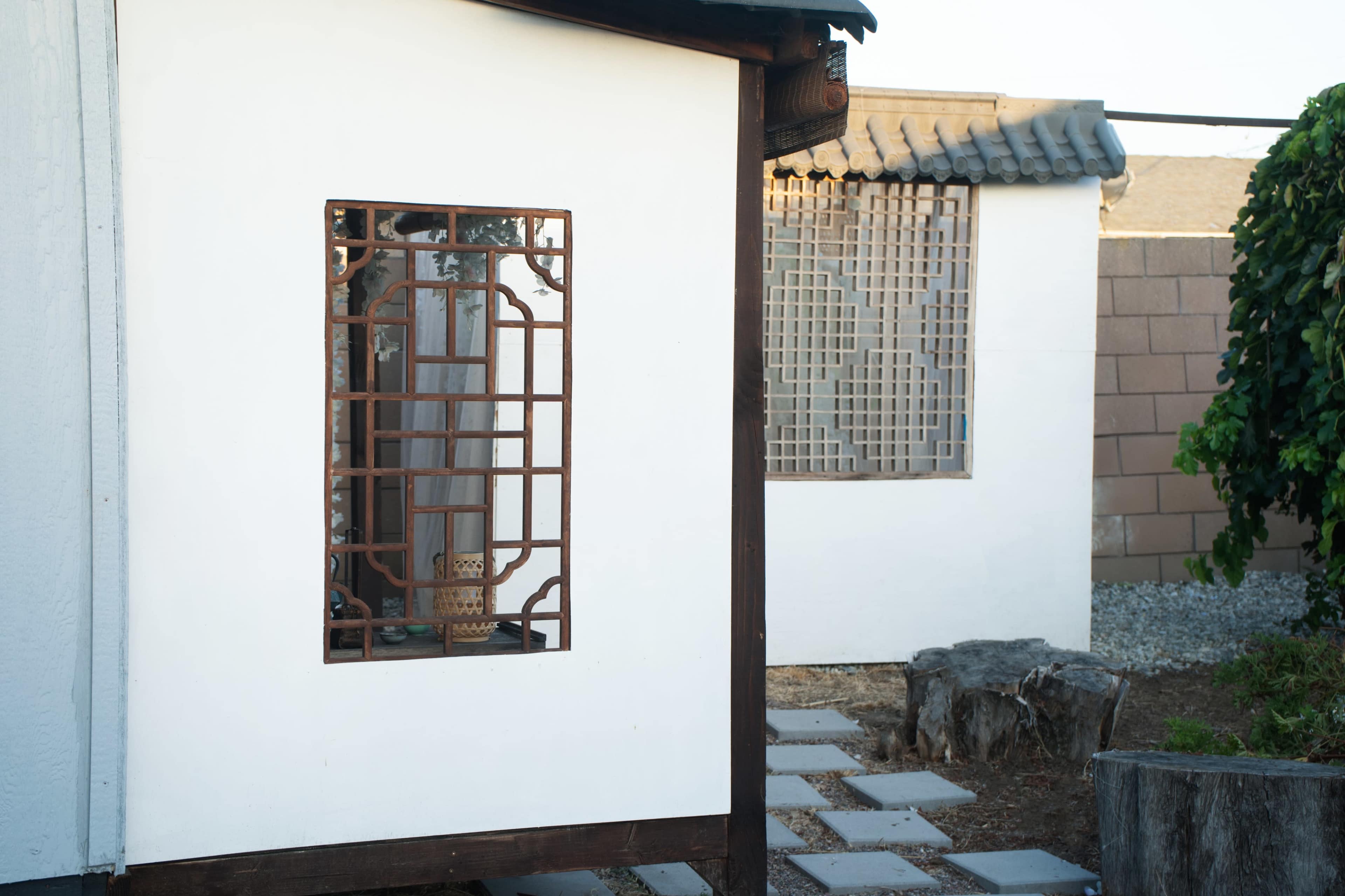 The image shows two structures with white walls and decorative lattice windows set in a garden area.