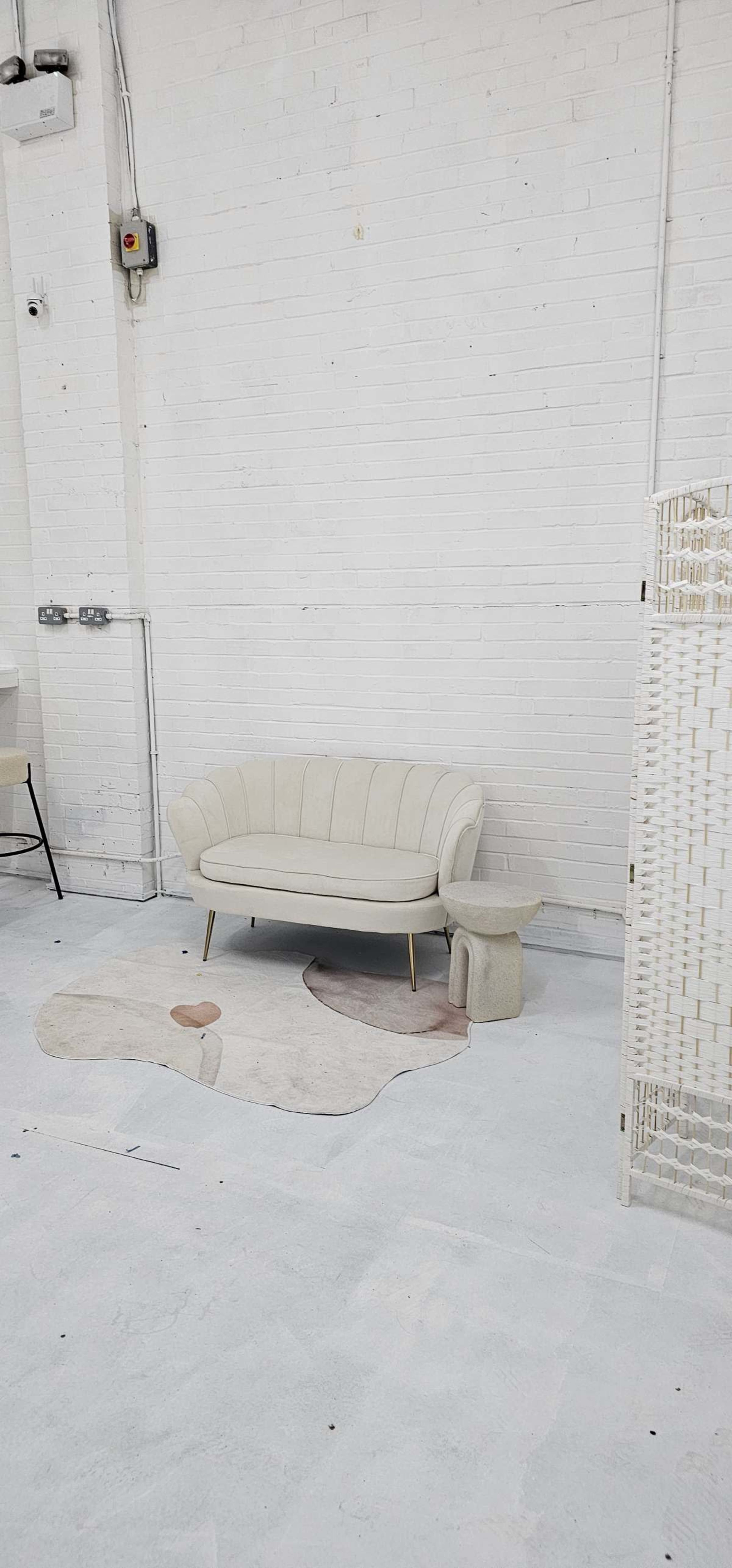 The image shows a light-colored sofa and a small stool on a patterned rug in a room with white brick walls and a minimalist design.