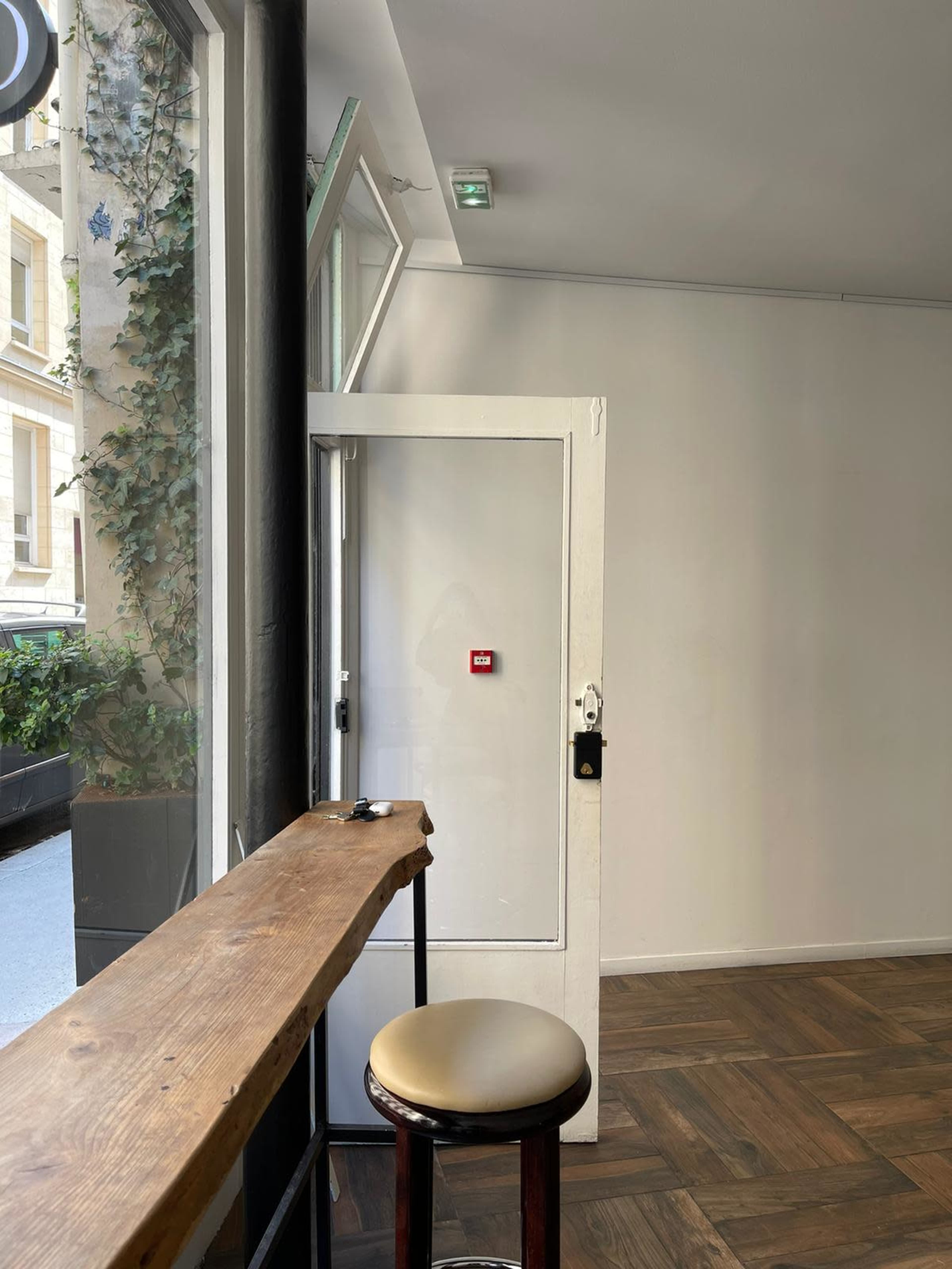 A wooden counter with a bar stool is positioned in front of an open door, leading to a street view through a large window.