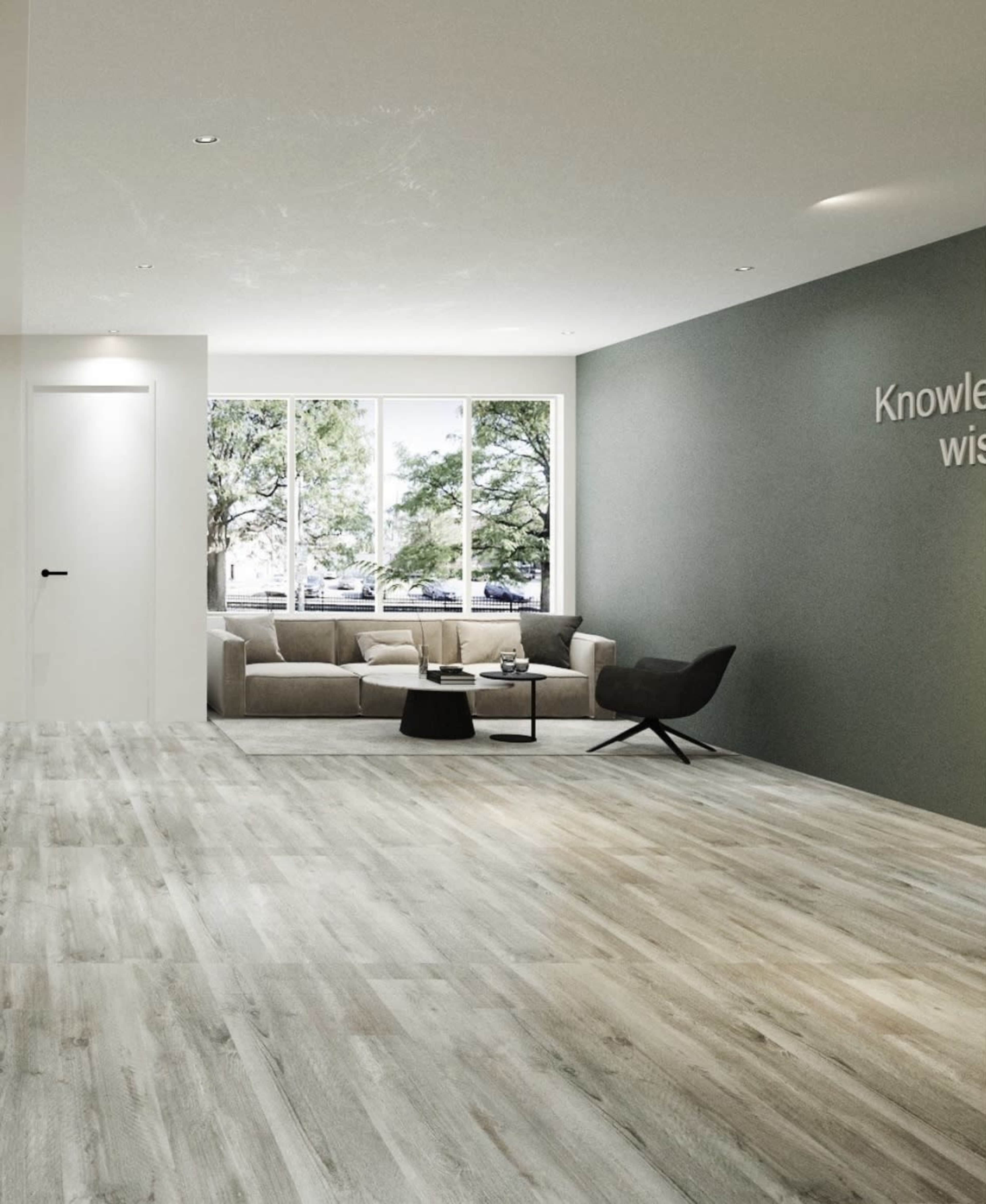 A spacious, modern room features a comfortable seating area with a couch and coffee table, large windows allowing natural light, and a wall with a motivational quote.