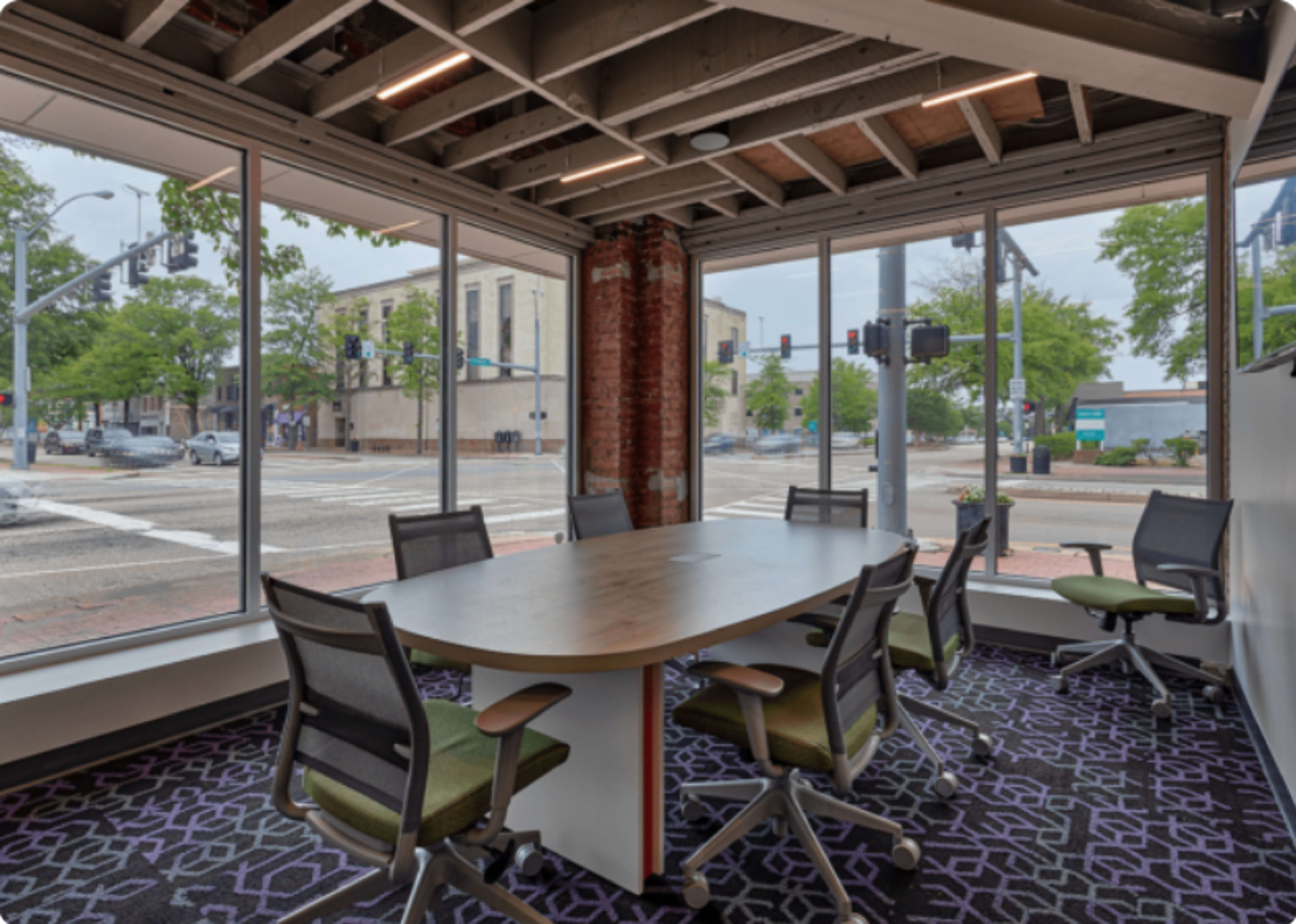 A modern conference room features a large table surrounded by ergonomic chairs, with large windows offering views of an urban intersection.