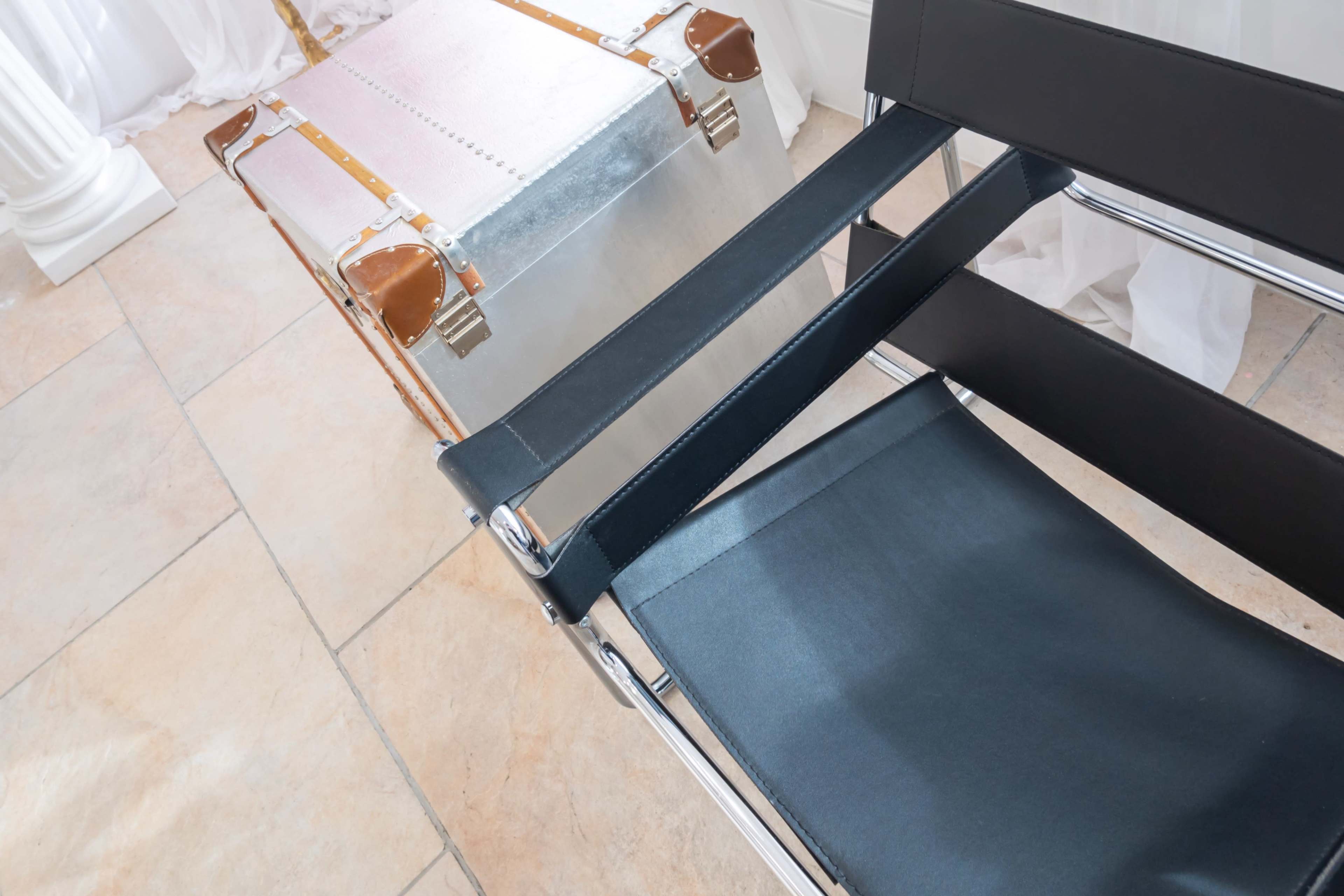 A black canvas director's chair is positioned beside a silver and brown vintage trunk on a tiled floor.