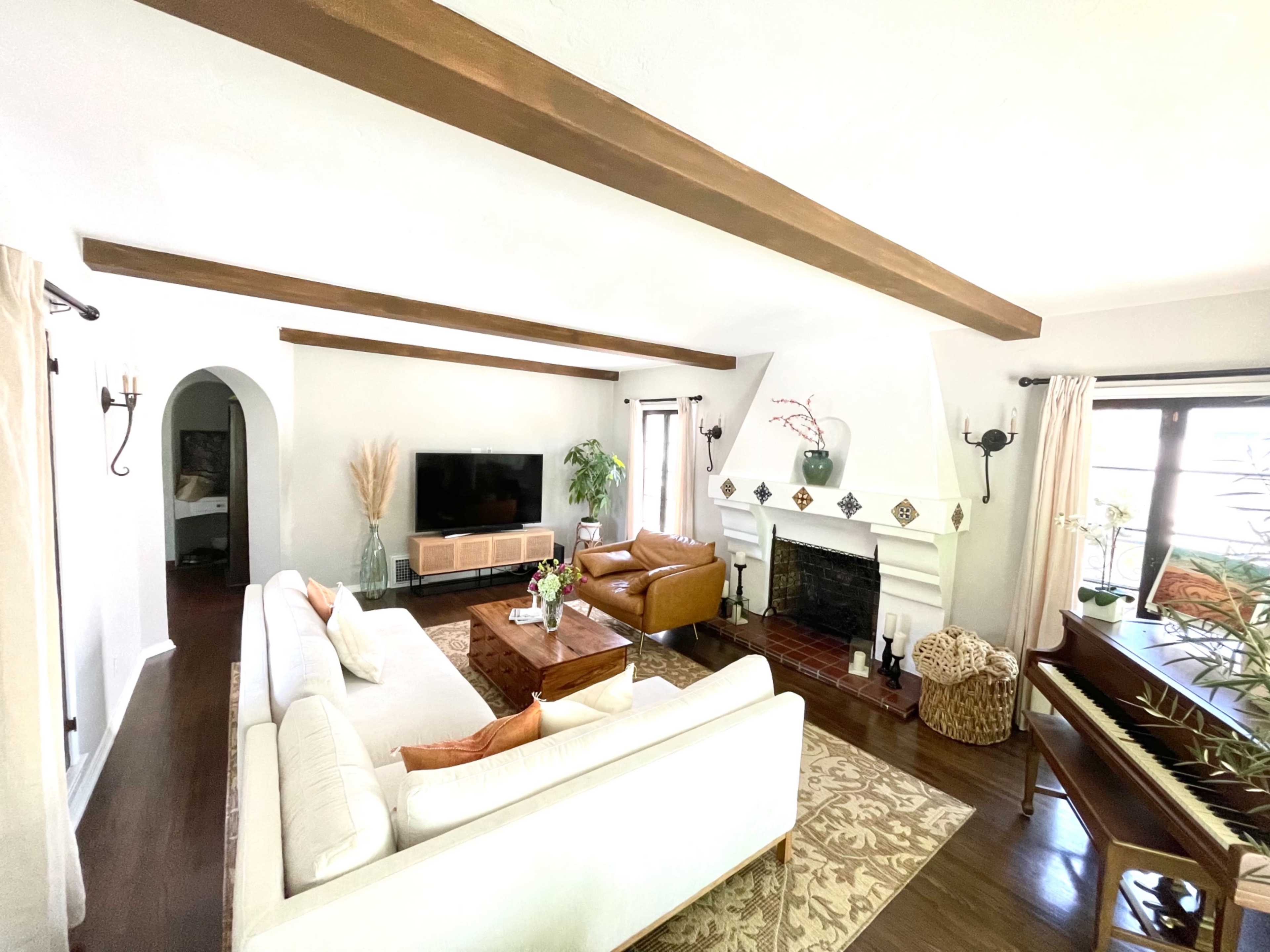 The living room features a white sofa, brown leather chair, and wooden coffee table arranged around a fireplace with decorative elements.