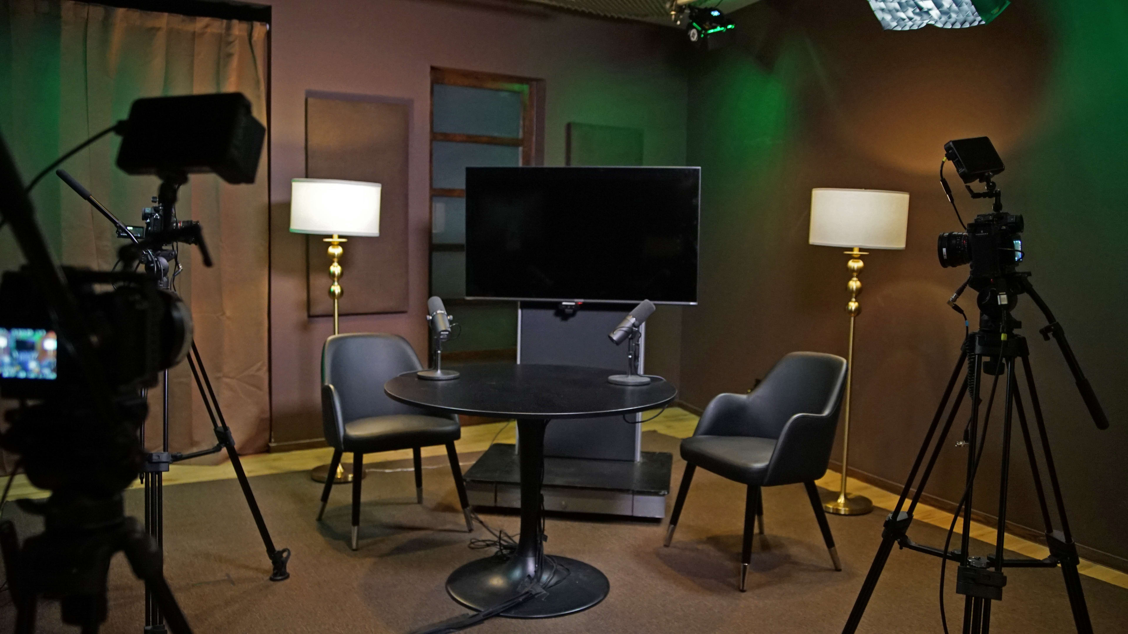 A small video recording studio with two chairs, a round table, and equipment set up for filming.