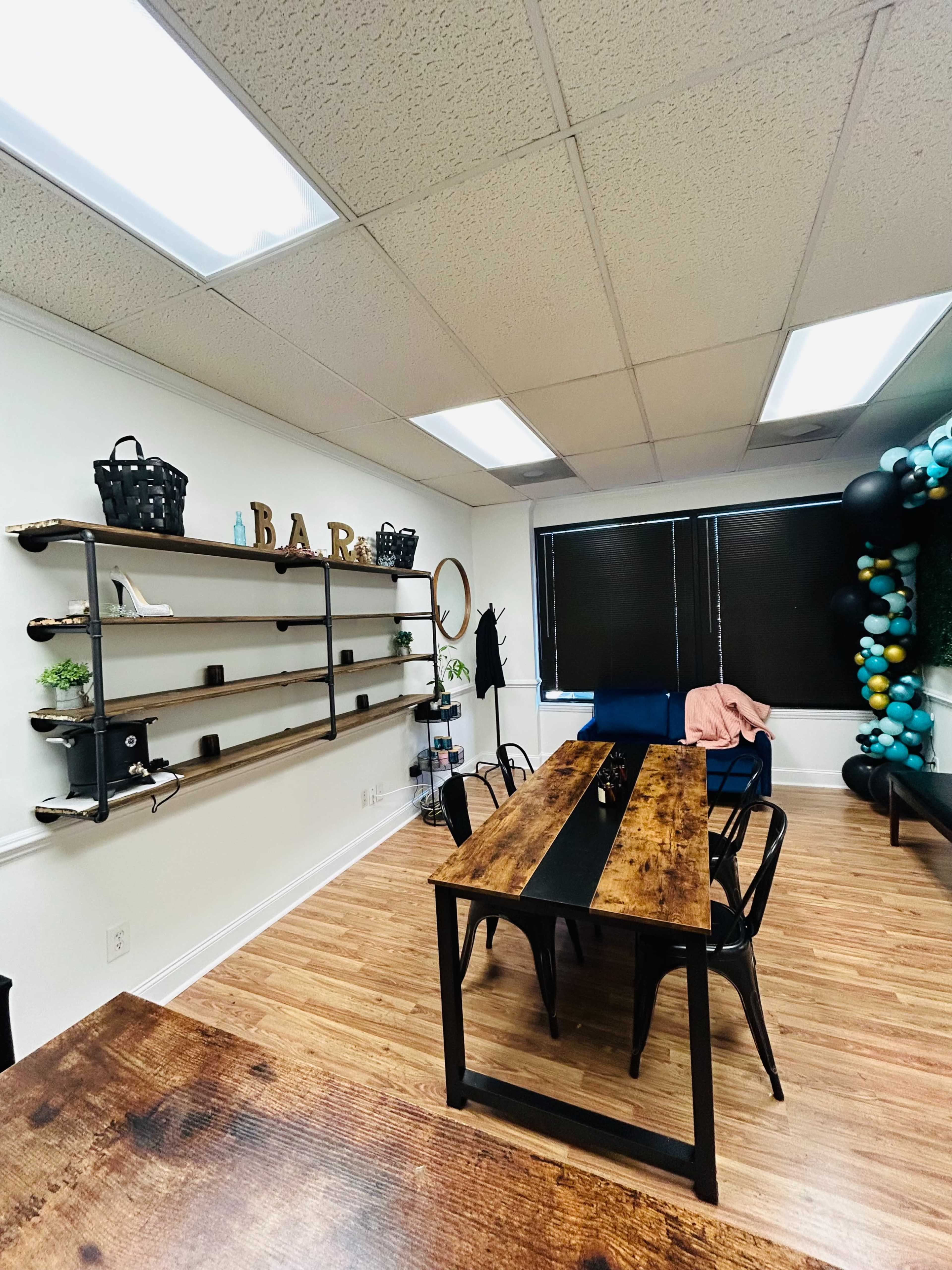 A modern office space featuring a wooden table, metal chairs, and shelves with decorative items, along with a wall adorned with the letters "BAR."