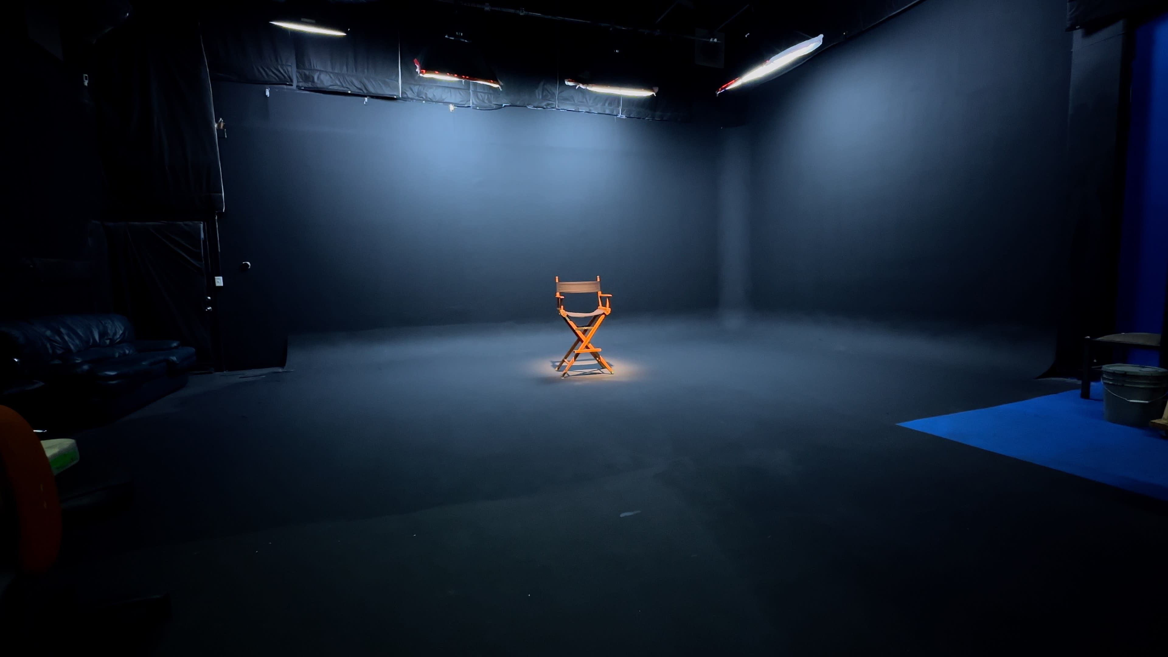 A solitary wooden director's chair is illuminated in the center of a dark, empty studio space.