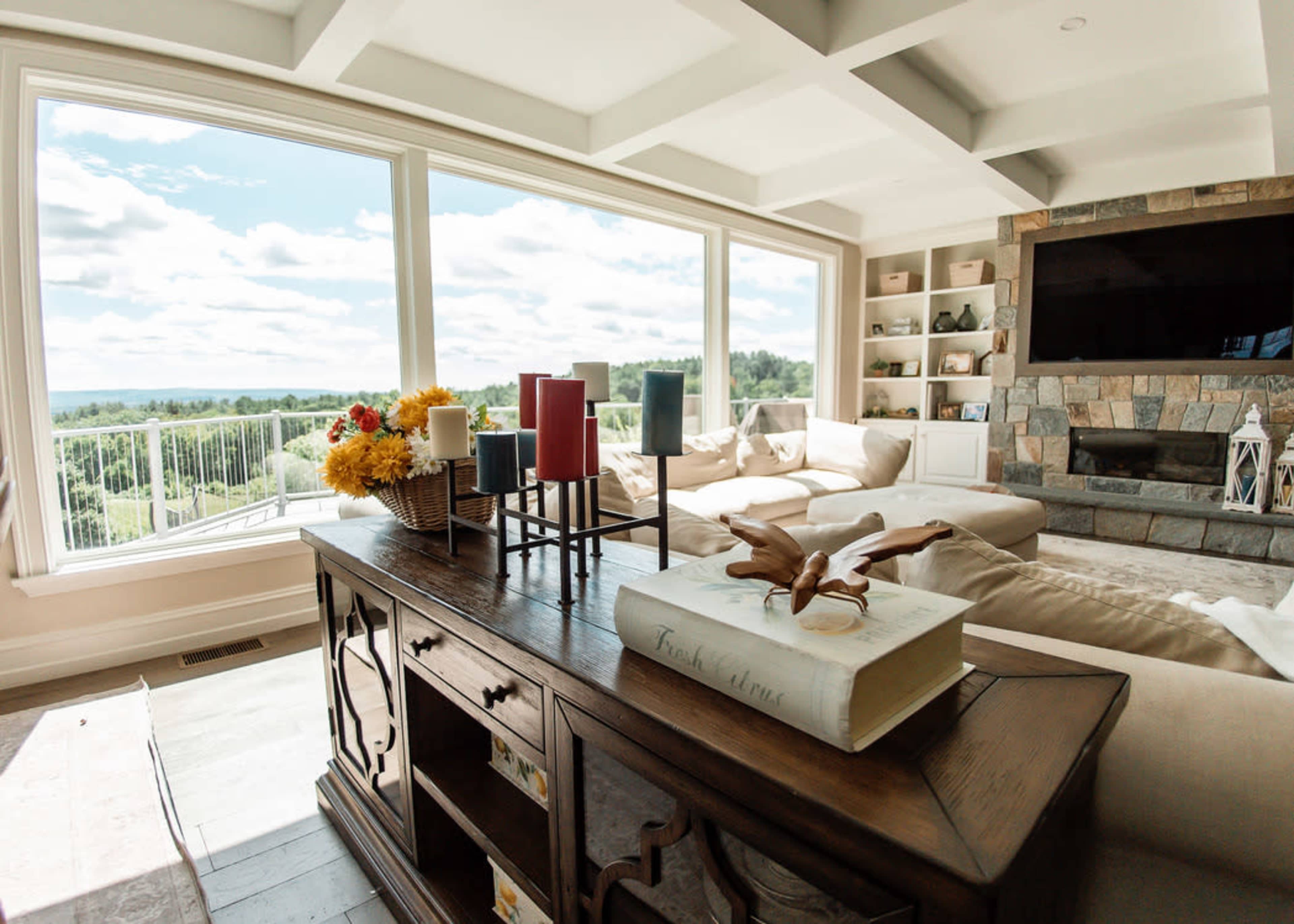 A spacious living room features large windows with a view, a comfortable sectional sofa, and a wooden coffee table adorned with decorative items.