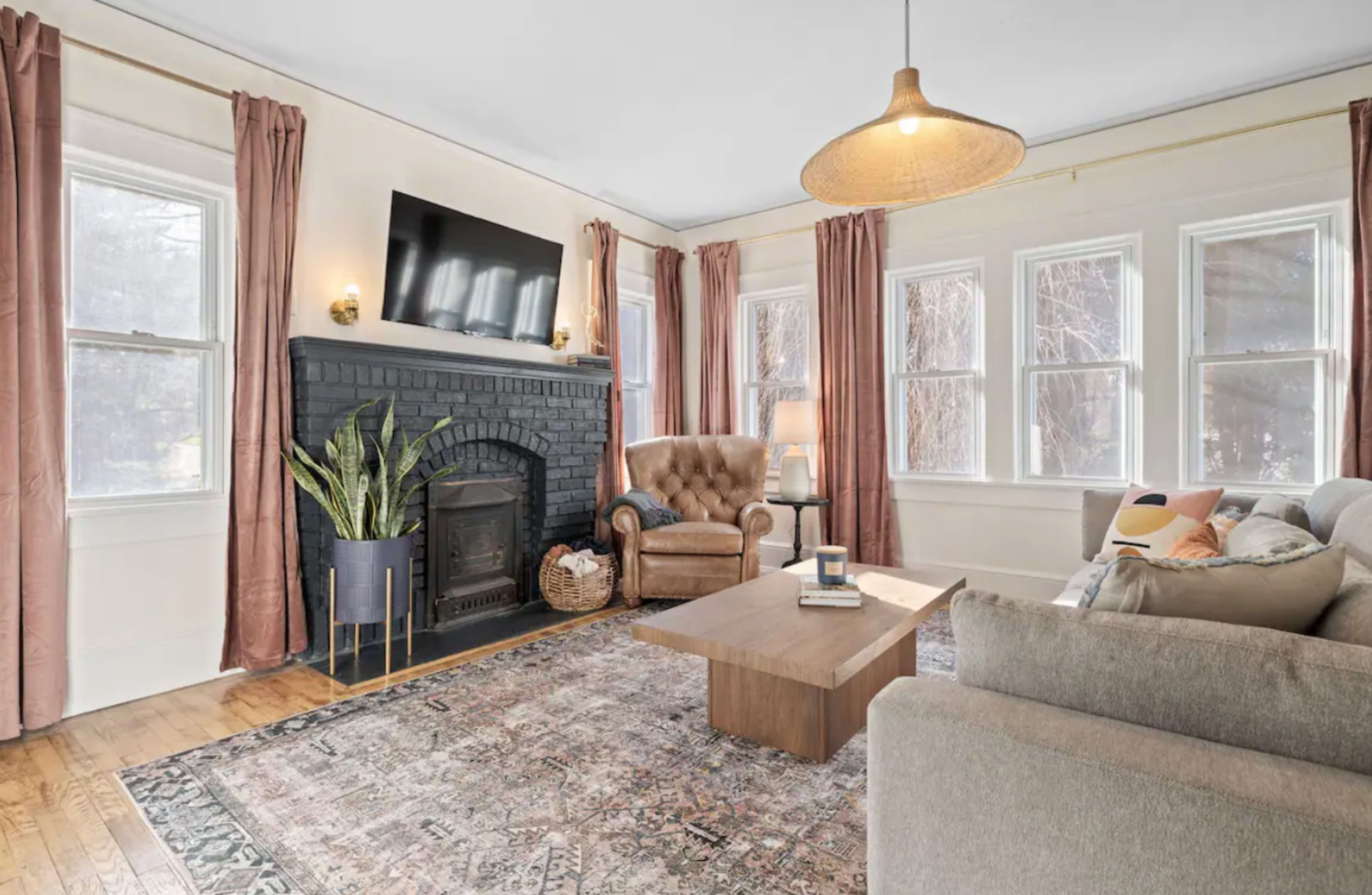The living room features a dark-brick fireplace, a large window, a sofa, an armchair, and a coffee table.