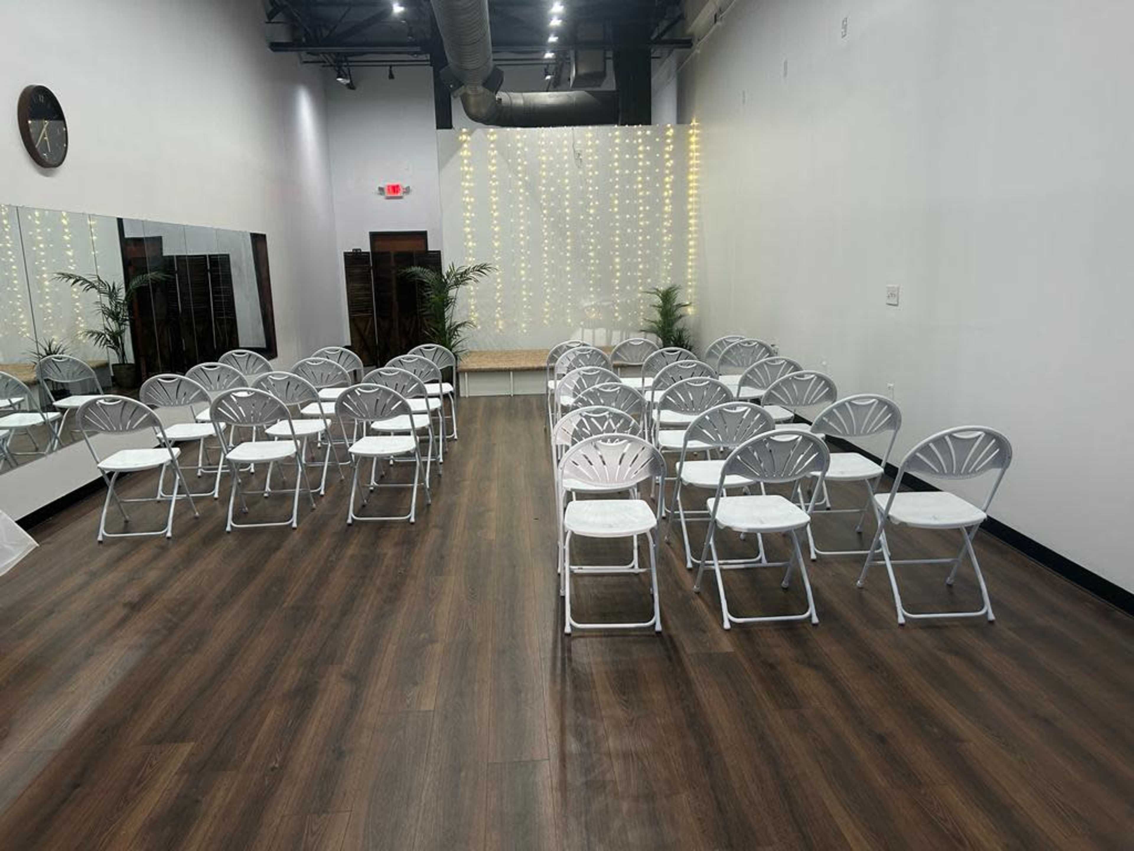 A spacious room arranged with white folding chairs facing a decorated backdrop of string lights.