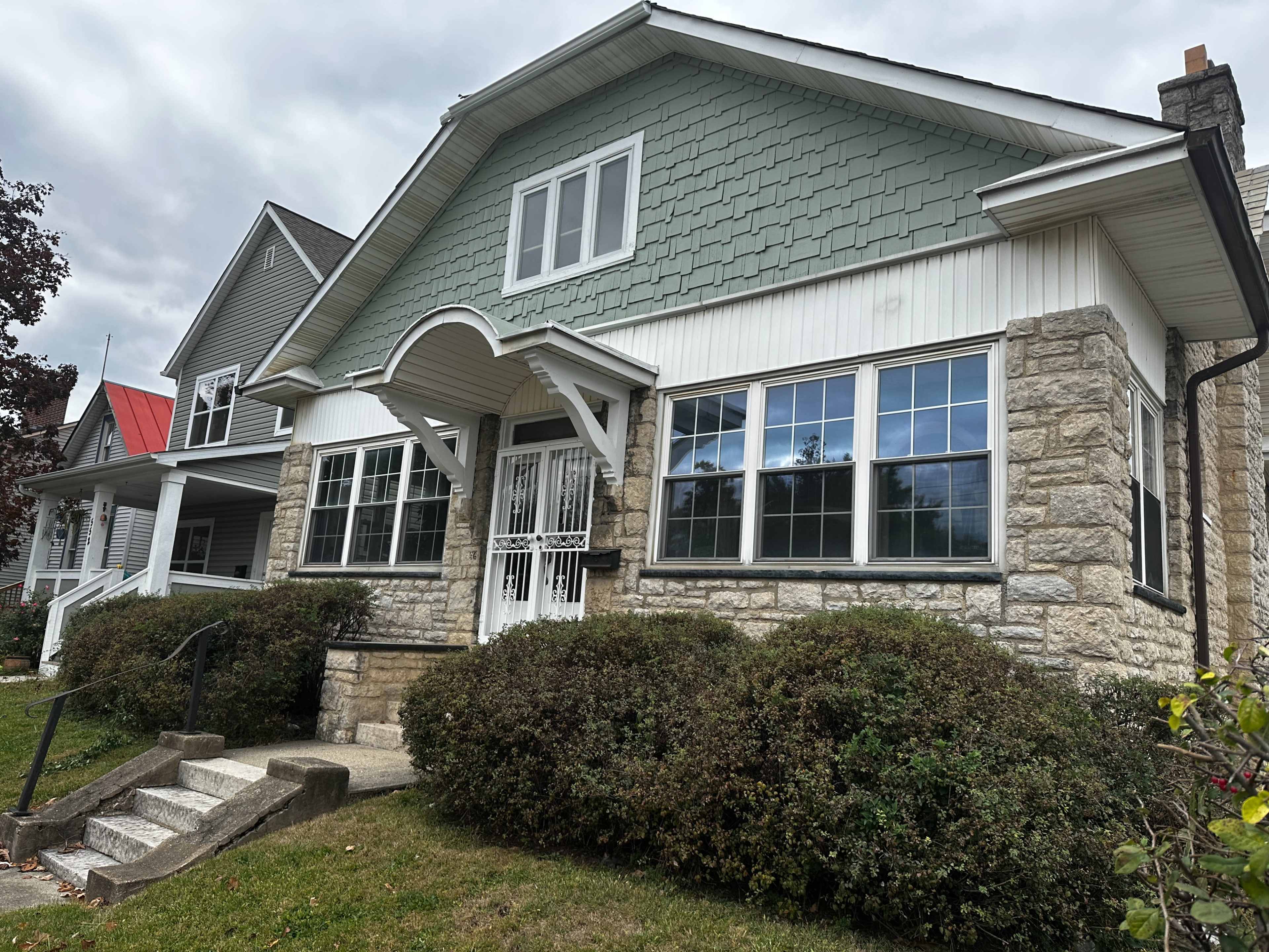 A two-story house with a green shingle roof, stone walls on the lower portion, and large front windows.