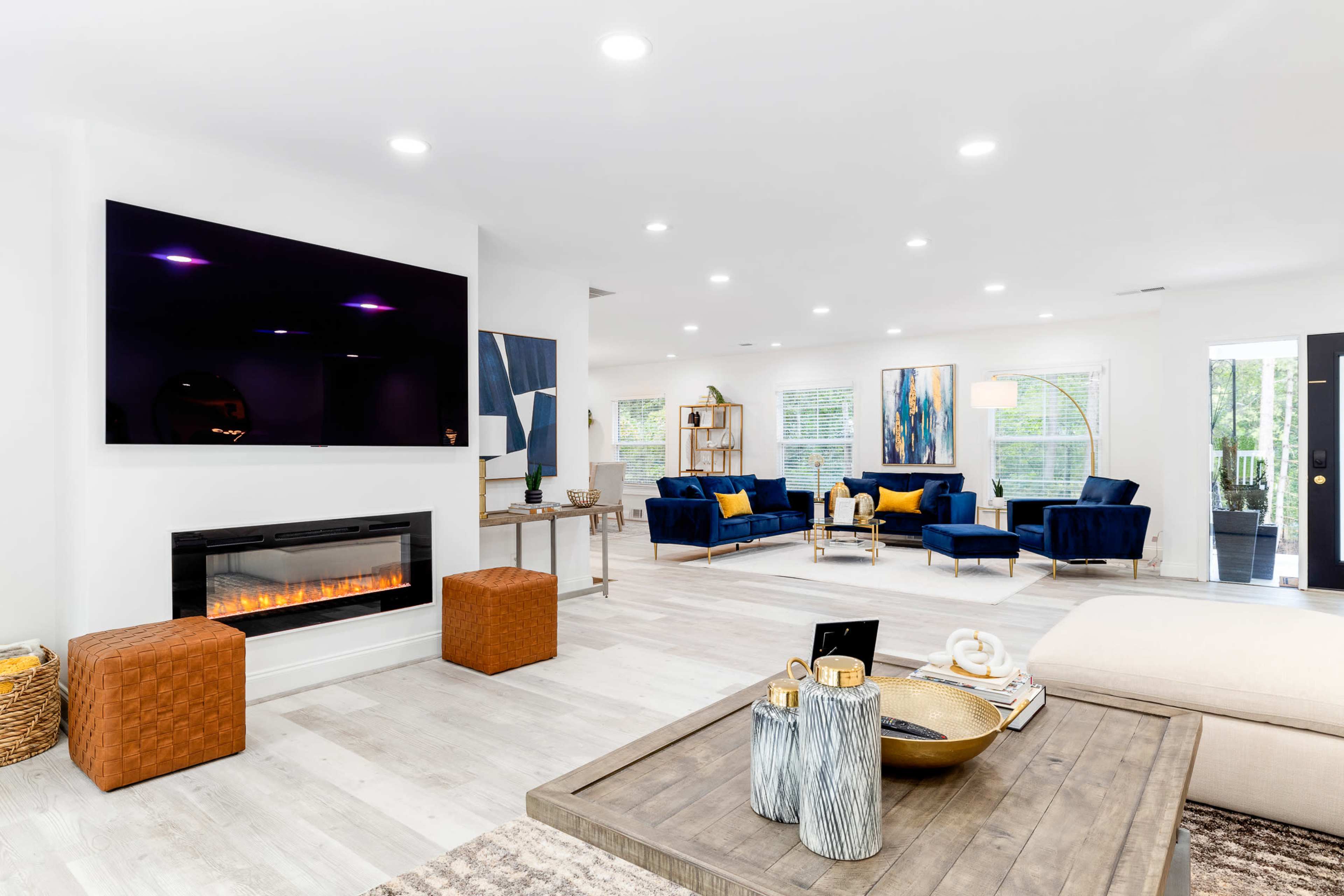 A modern living room featuring a wall-mounted television, an electric fireplace, and blue seating with yellow accents around a coffee table.