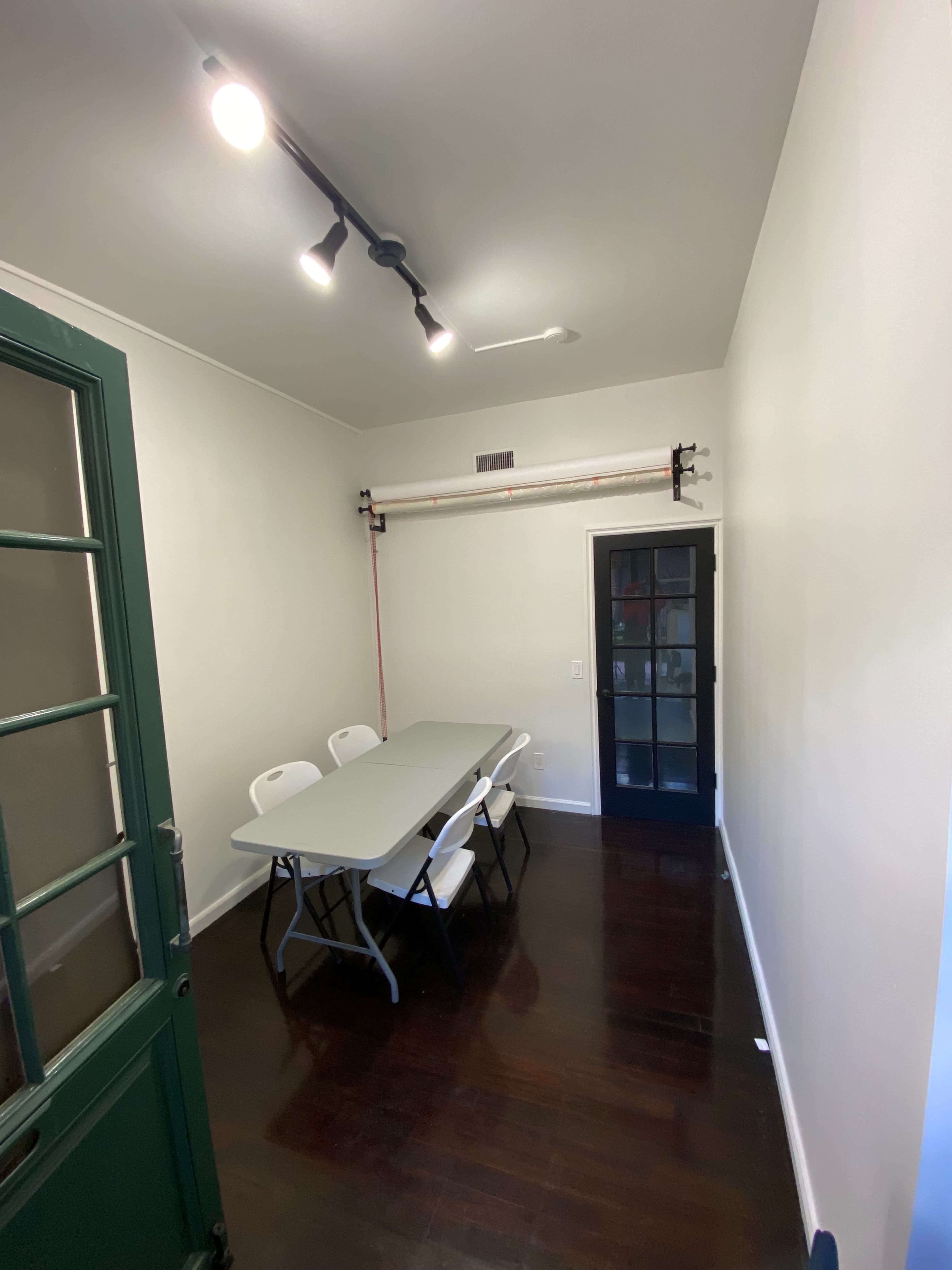 The image shows a small room with a table and several chairs arranged inside, and a door leading to another area.