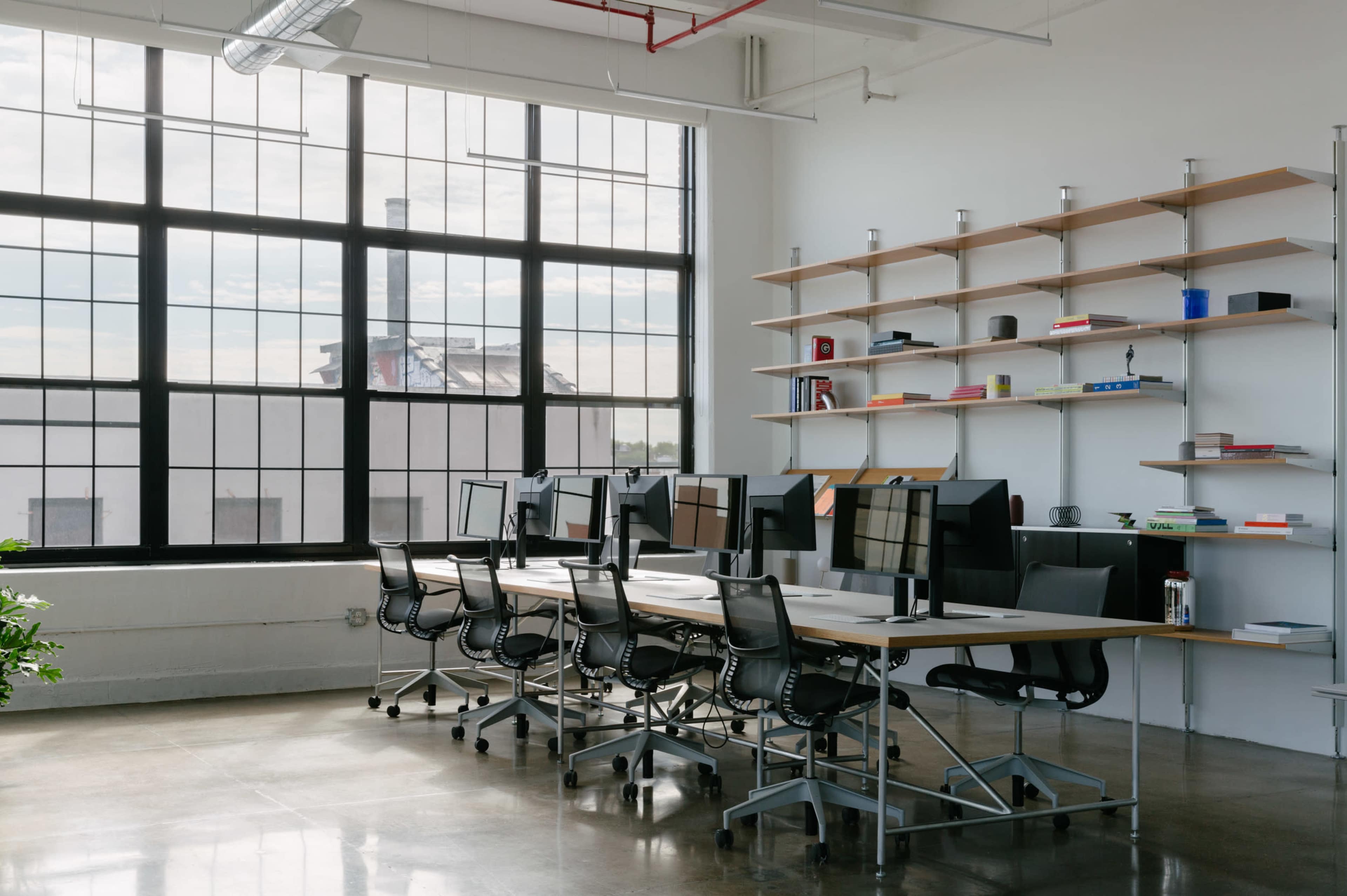 A modern office space with several desks equipped with computers and large windows allowing natural light to fill the room.