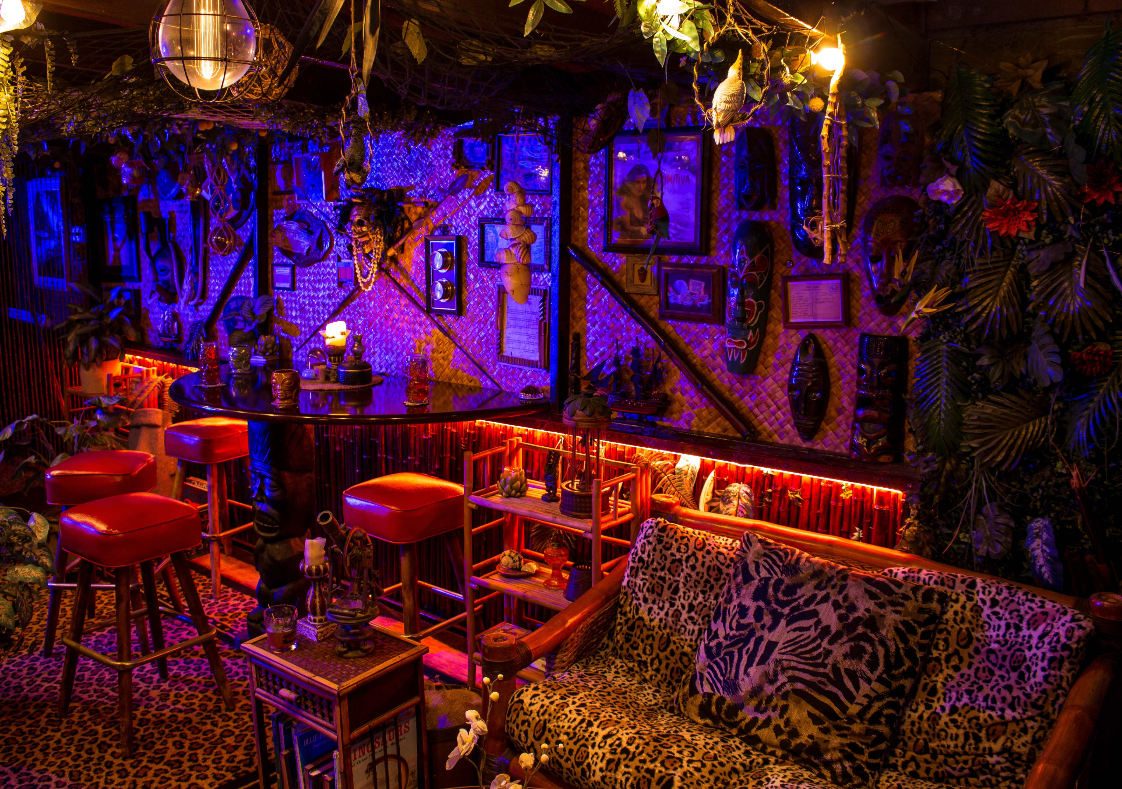 The scene features a vibrant tiki bar adorned with tropical decor, illuminated by colorful lighting and surrounded by lush foliage.