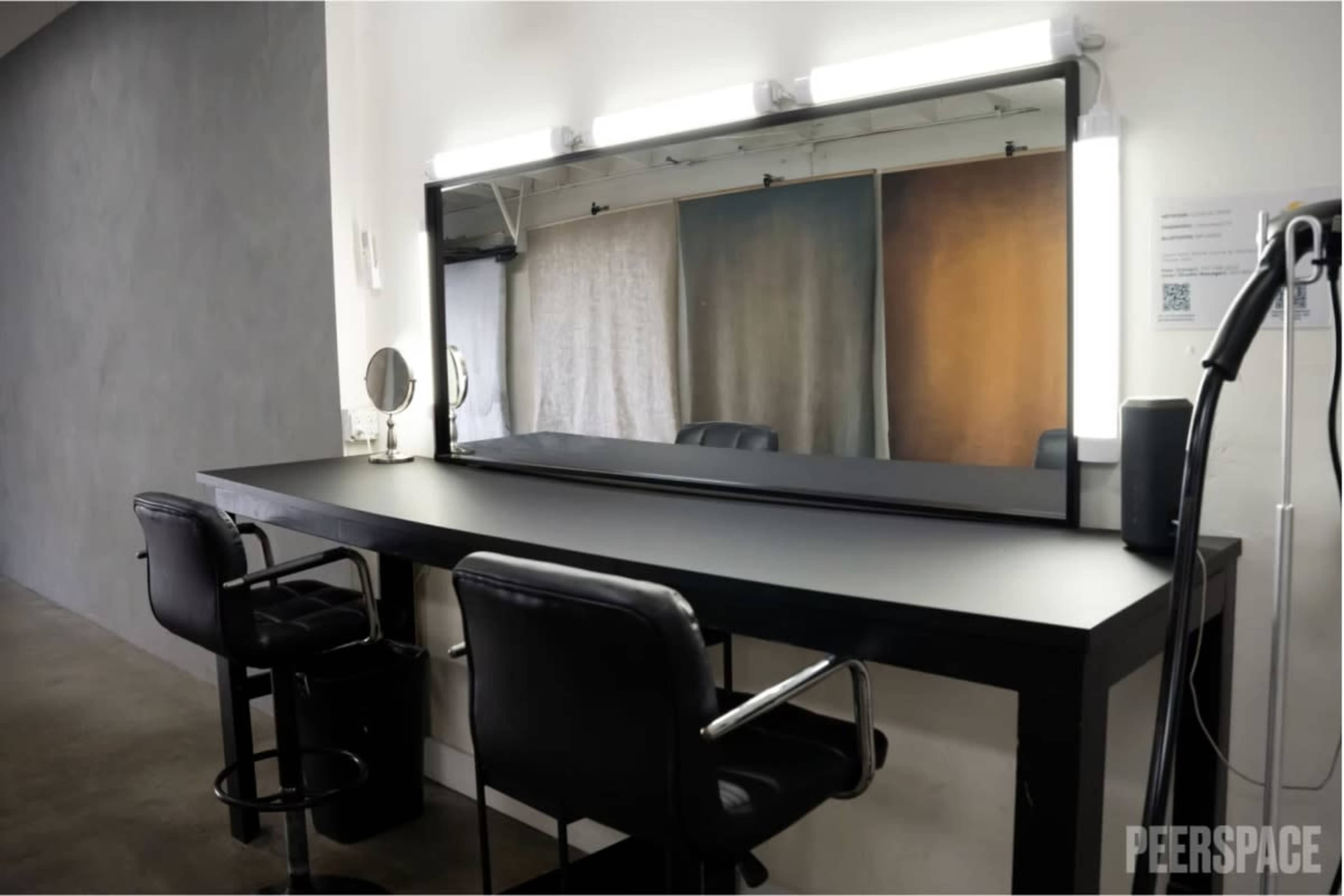 The image shows a modern makeup vanity area with a long mirror, two black chairs, and a minimalist design.