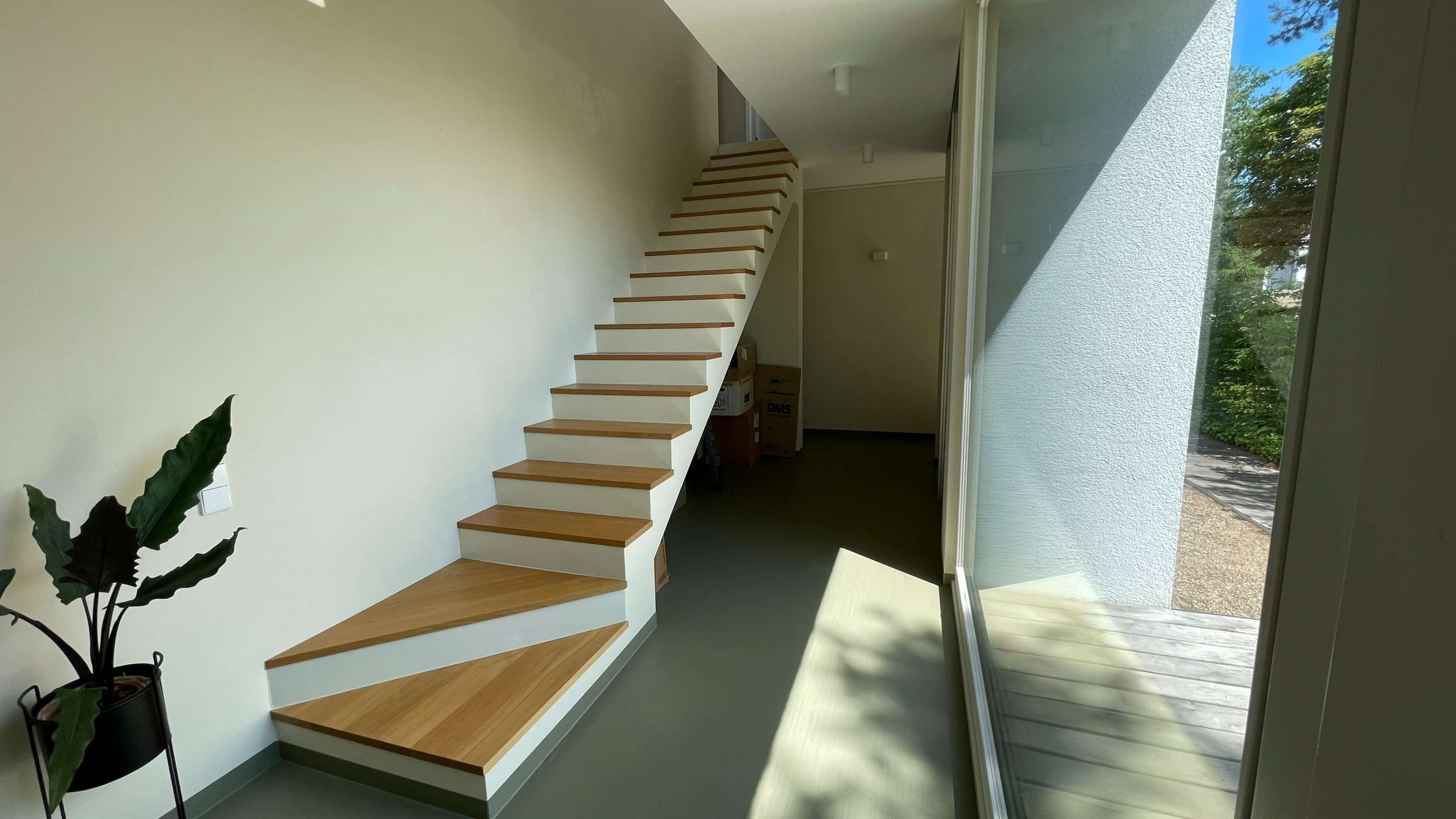 A modern interior featuring a wooden staircase leading to a second floor, with large windows providing natural light.