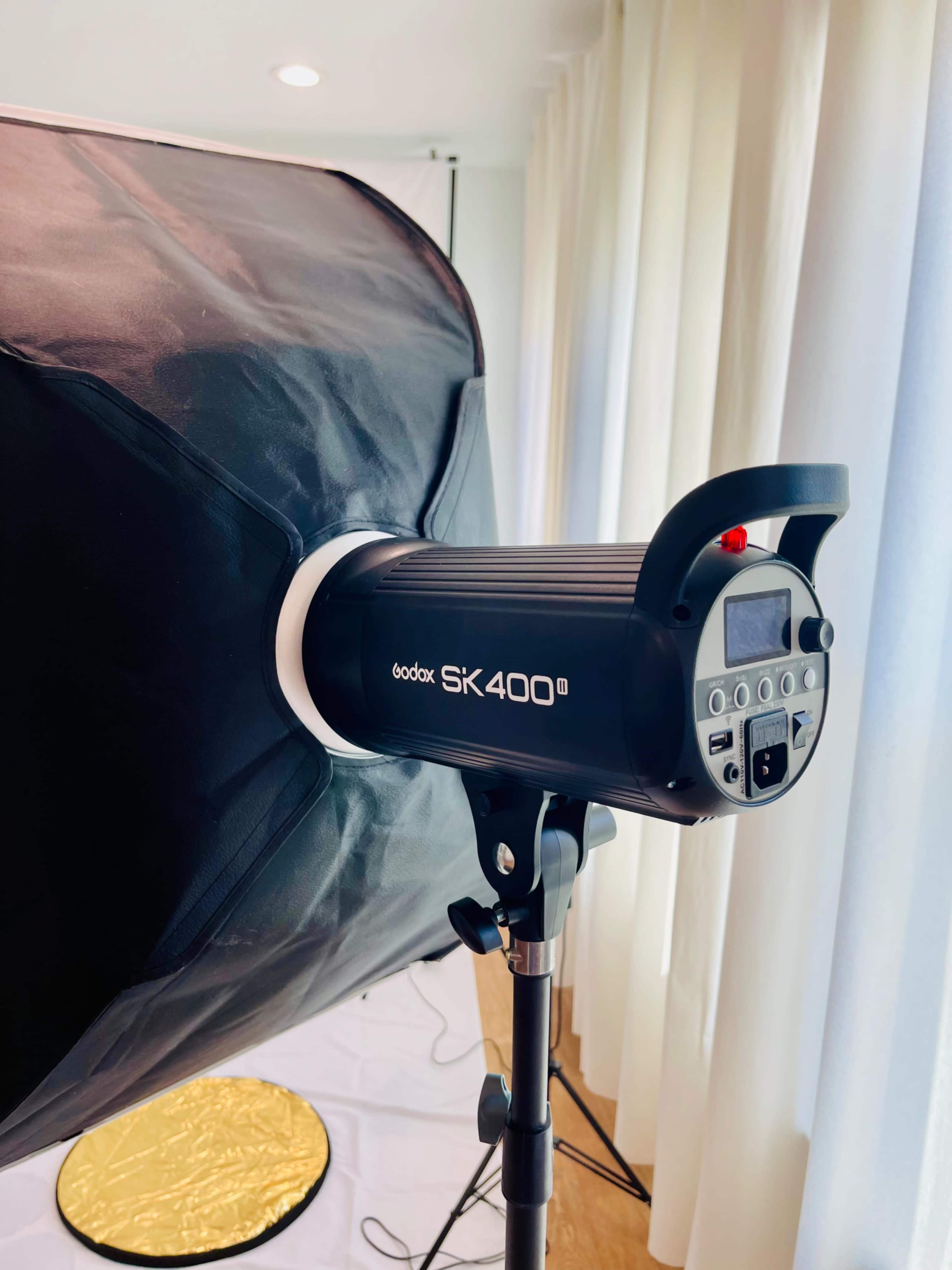 A Godox SK400II studio light mounted on a stand, with softbox and white curtains in the background.