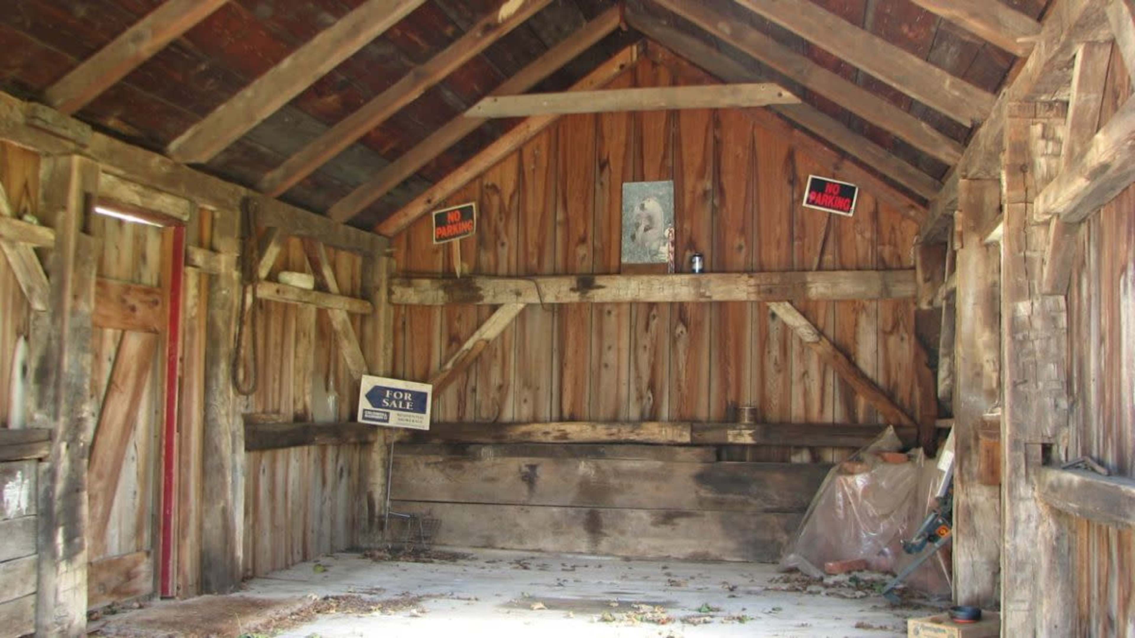The interior of a rustic wooden shed features bare walls, a few shelves, and signs indicating "For Sale" and warnings.