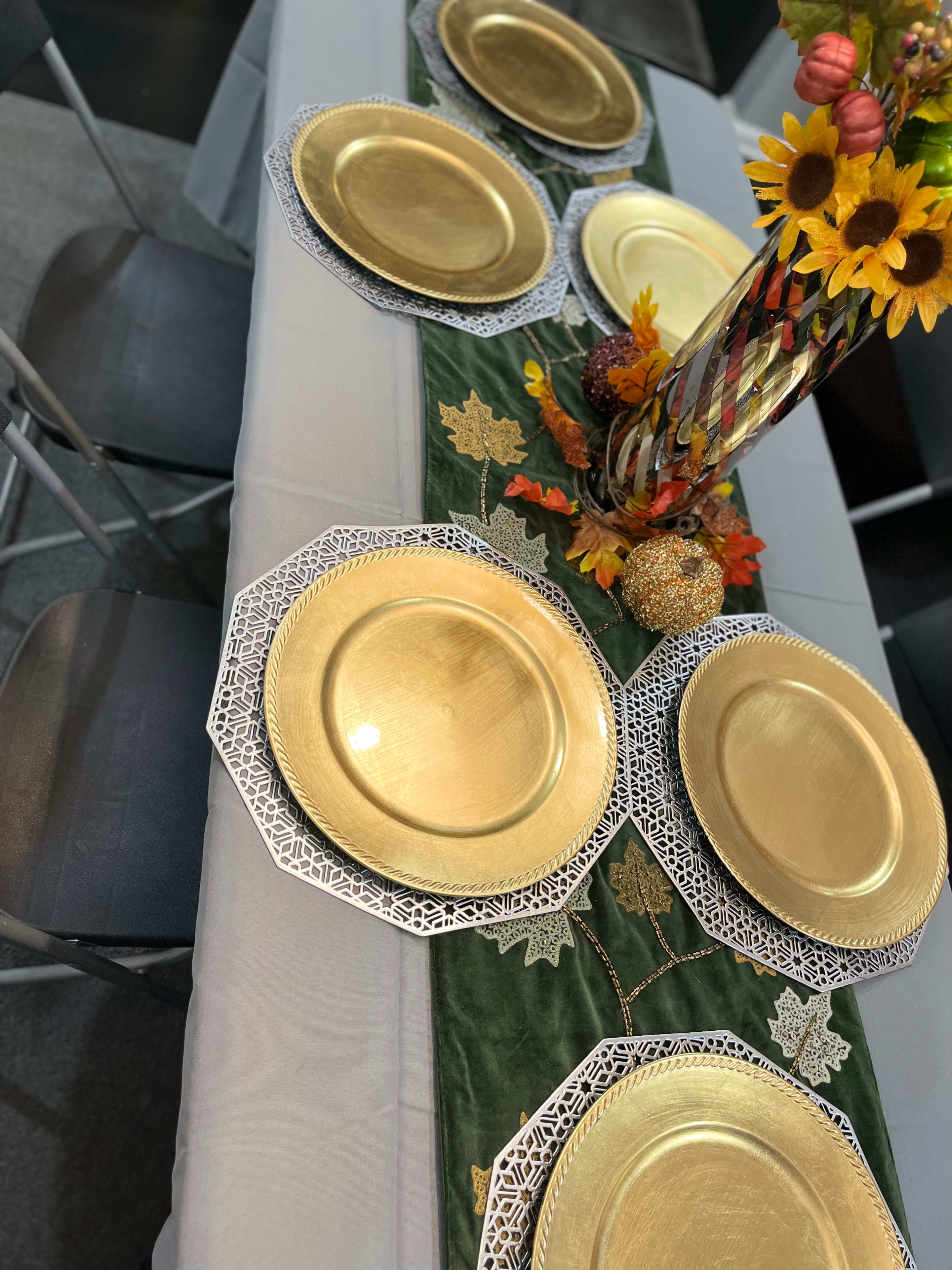 A dining table set with gold plates, a green table runner adorned with leaves, and a floral centerpiece featuring sunflowers and decorative items.