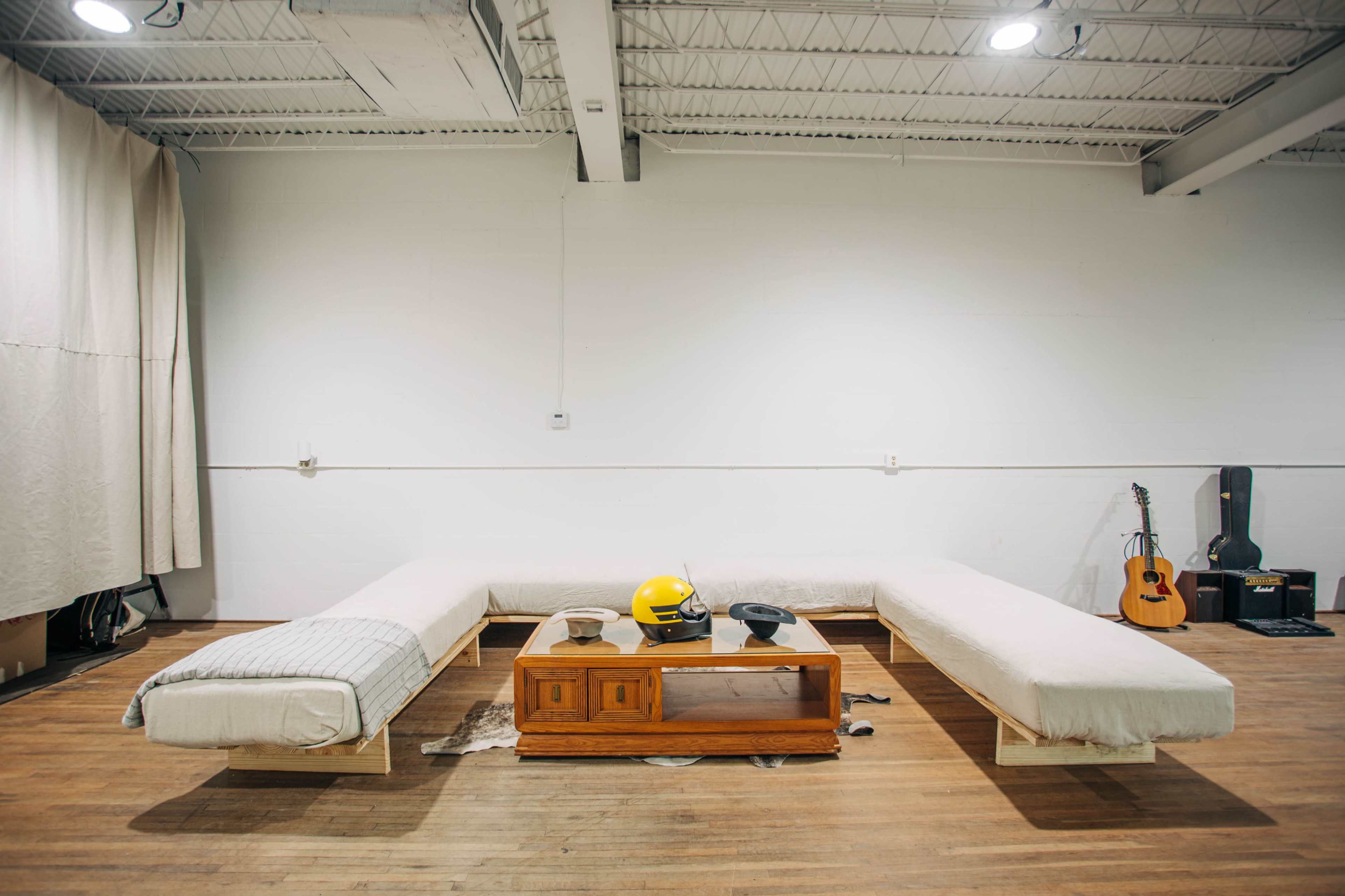 A minimalist interior with two elongated, low couches facing a wooden coffee table, a yellow helmet, and a black telephone, accompanied by a guitar leaning against the wall.