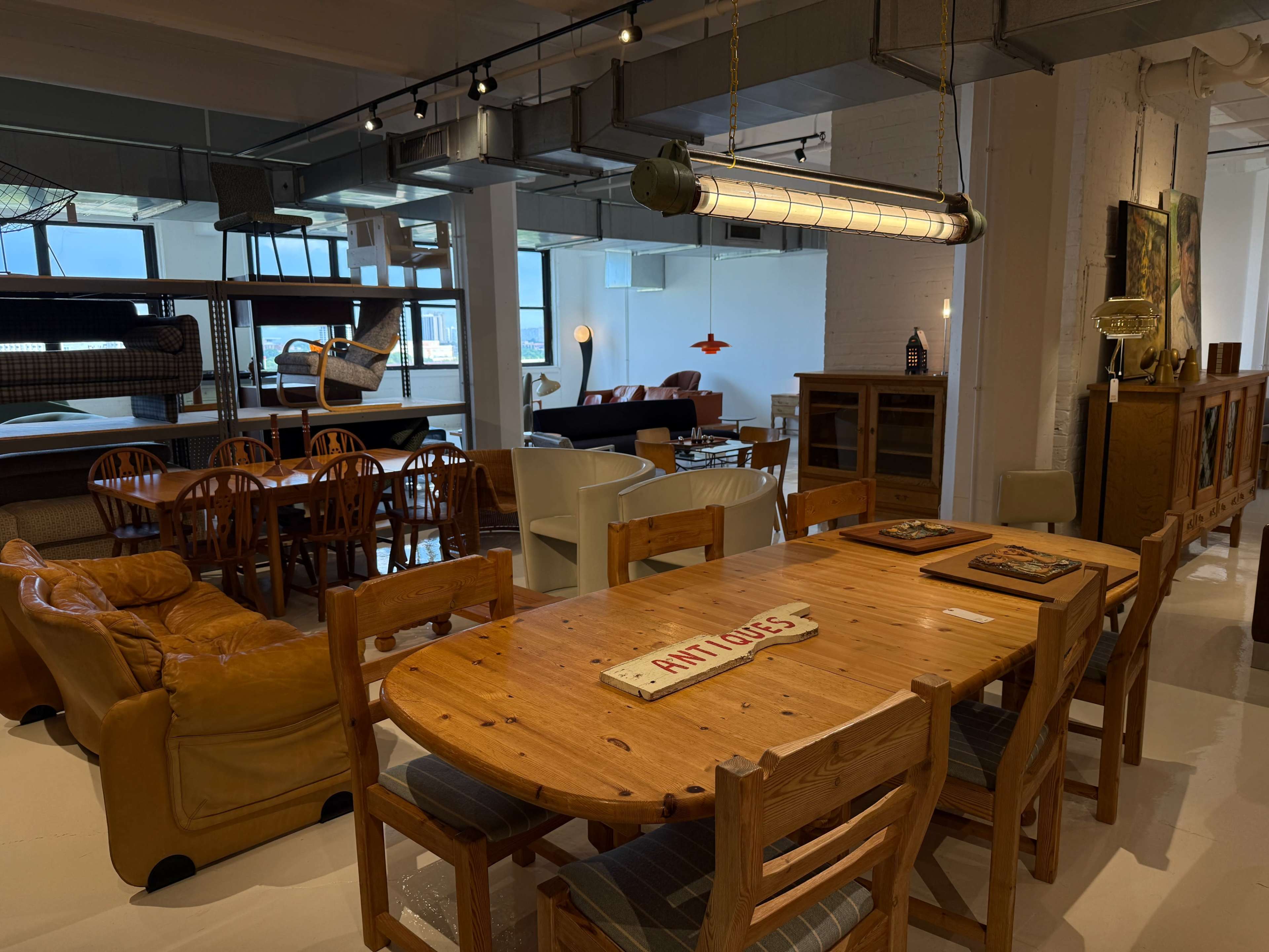 The image depicts a modern interior space featuring a variety of furniture, including a wooden dining table, chairs, and couches, alongside decorative items and large windows.