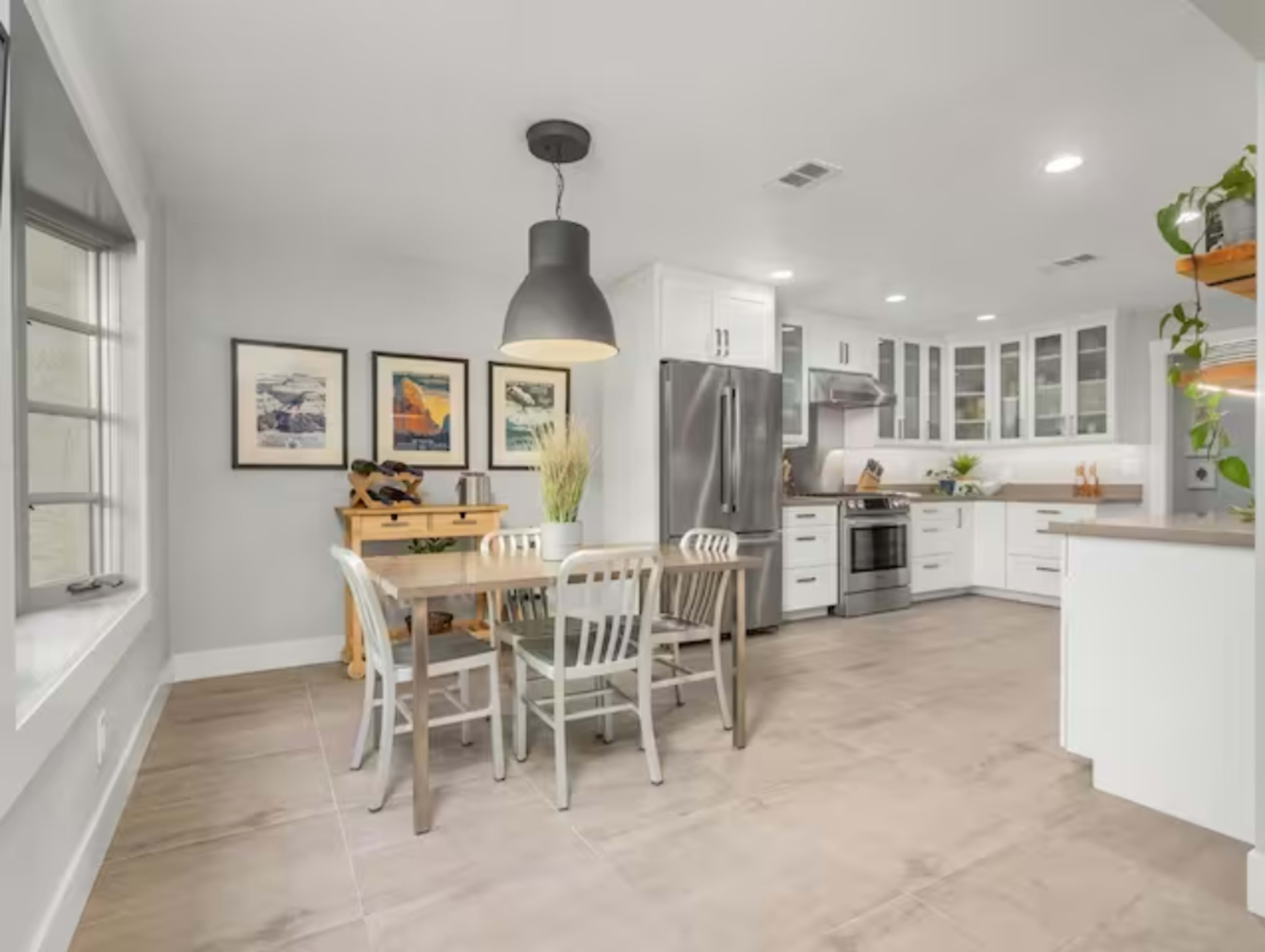 A modern kitchen features a dining table with four chairs, stainless steel appliances, and white cabinetry.