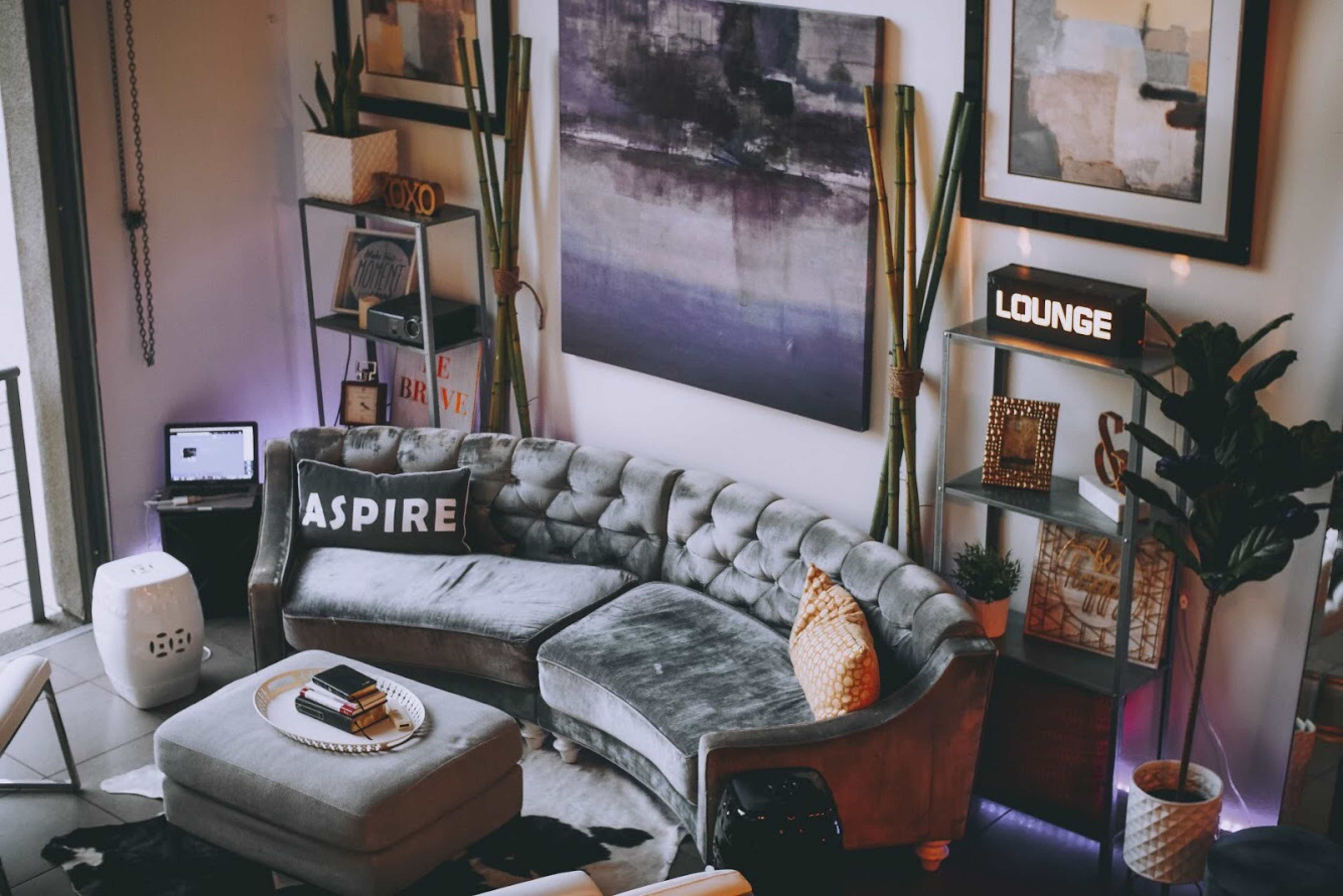 A modern living room with a gray sectional sofa, decorative cushions, a round coffee table, and wall shelves displaying various decor items.