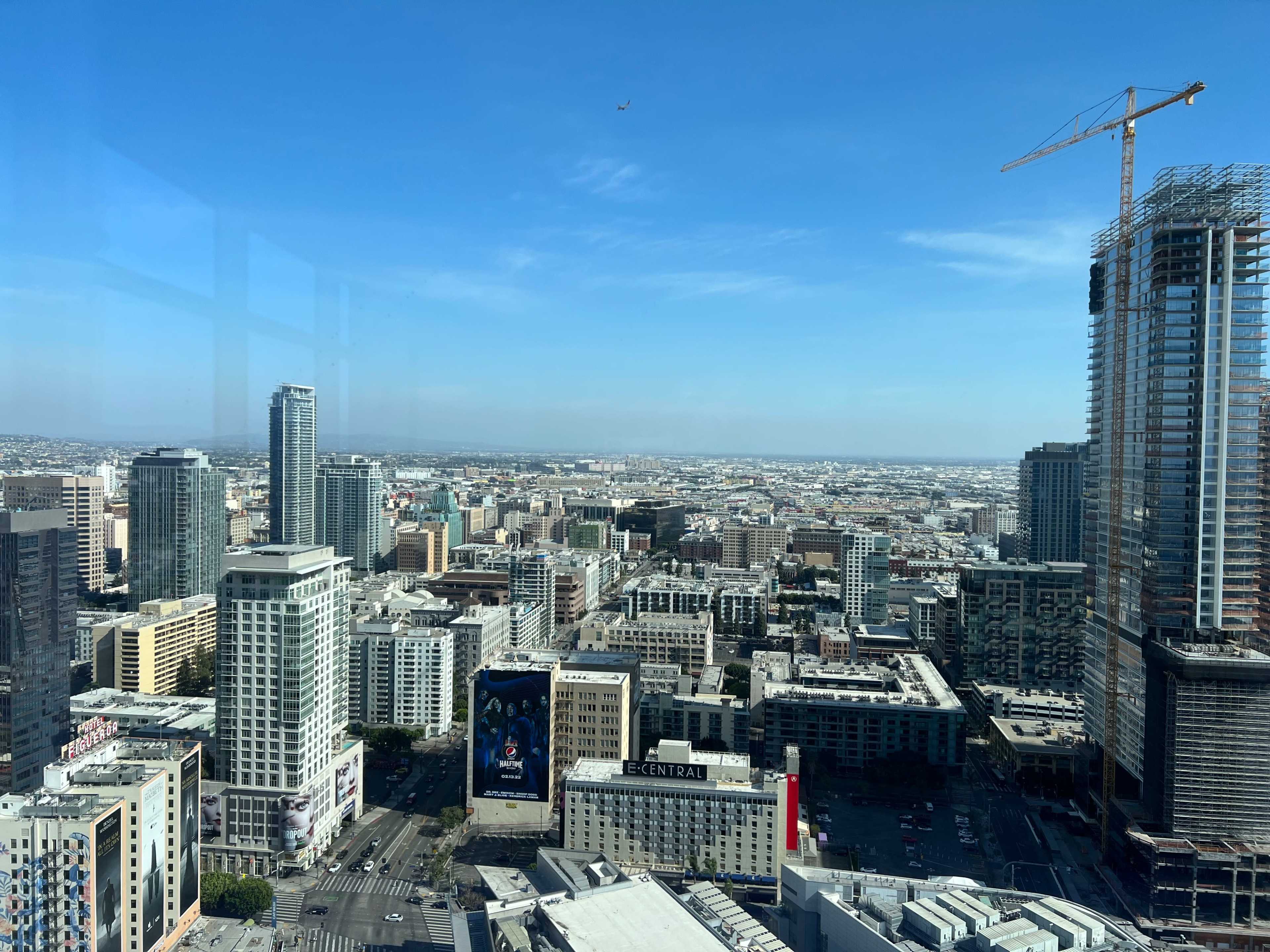 A high-angle view of a city skyline with various buildings, streets, and a construction site under a clear blue sky.