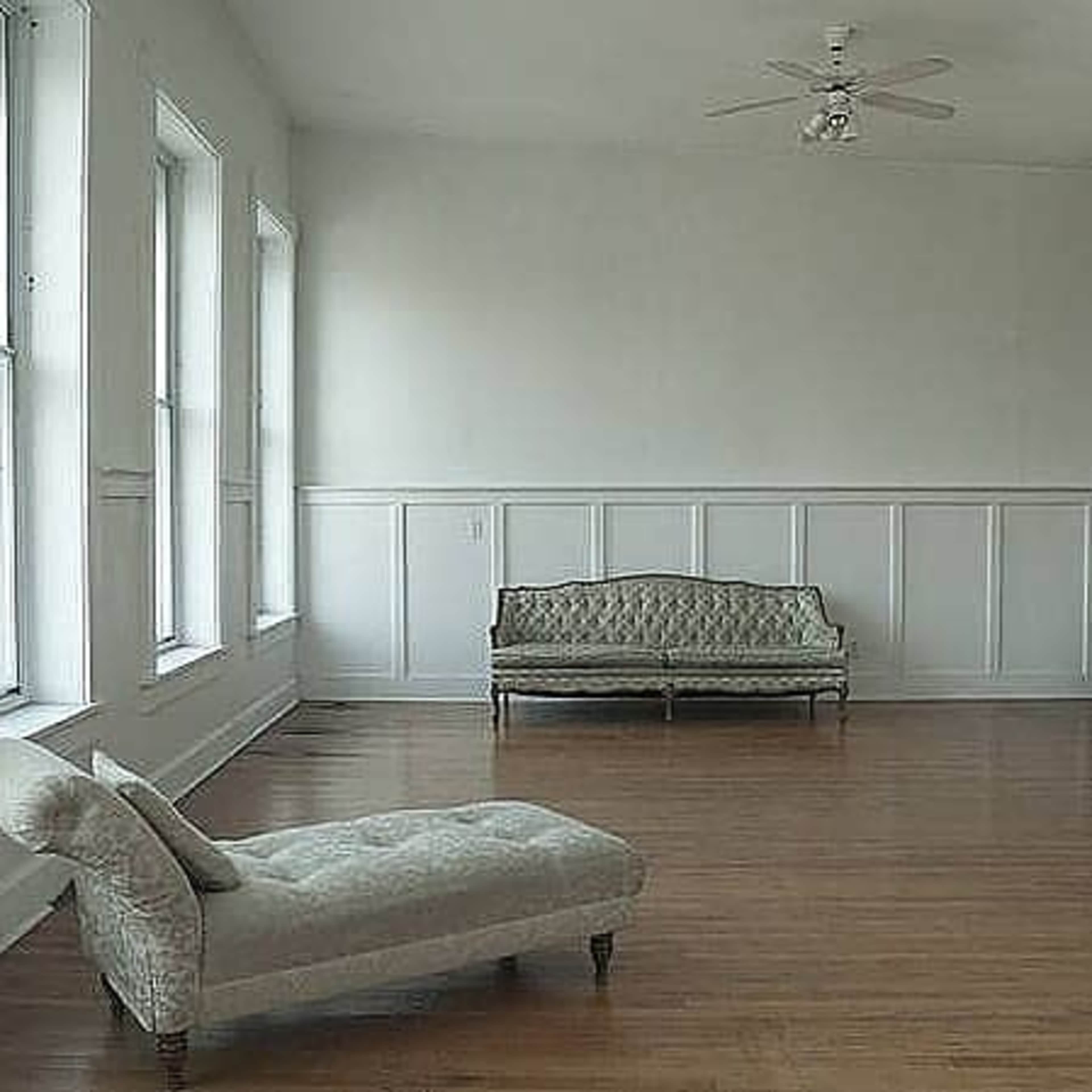 The room features a chaise lounge and a sofa against a wall of large windows with wooden flooring.