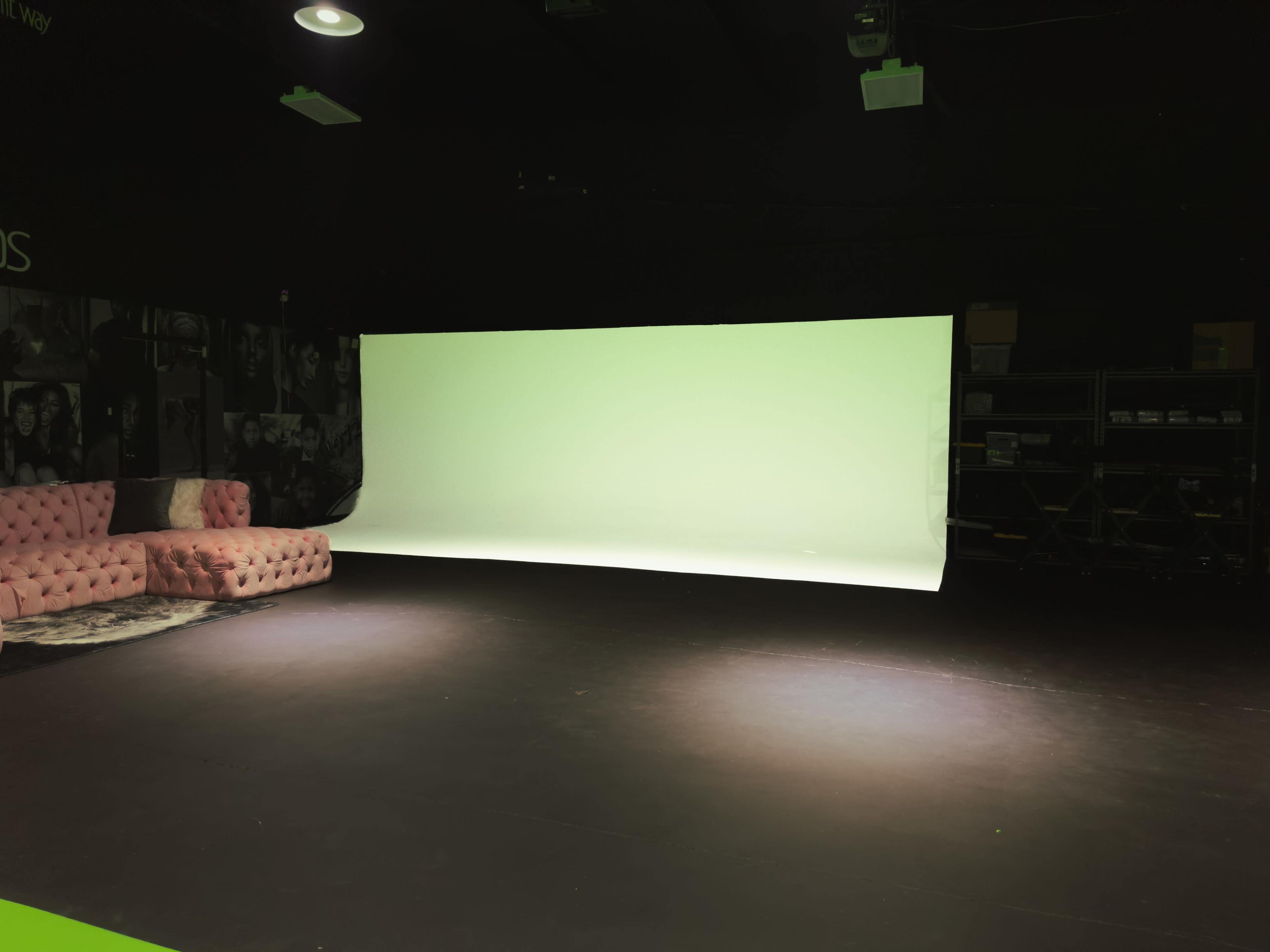 An empty studio space with a pink tufted couch and a large green backdrop illuminated in the center.
