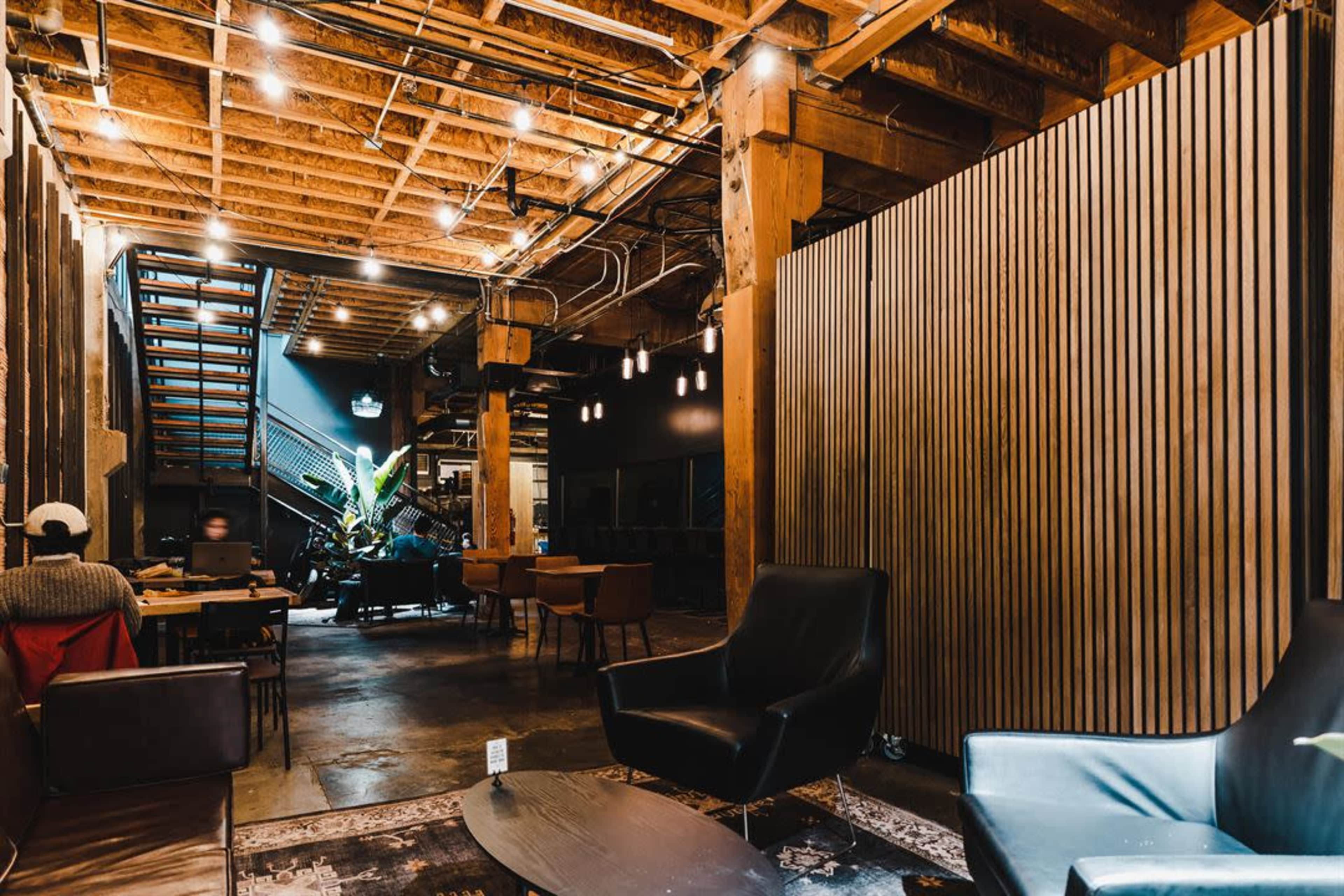 The interior features a modern workspace with wooden beams, seating areas, and a staircase leading to an upper level.