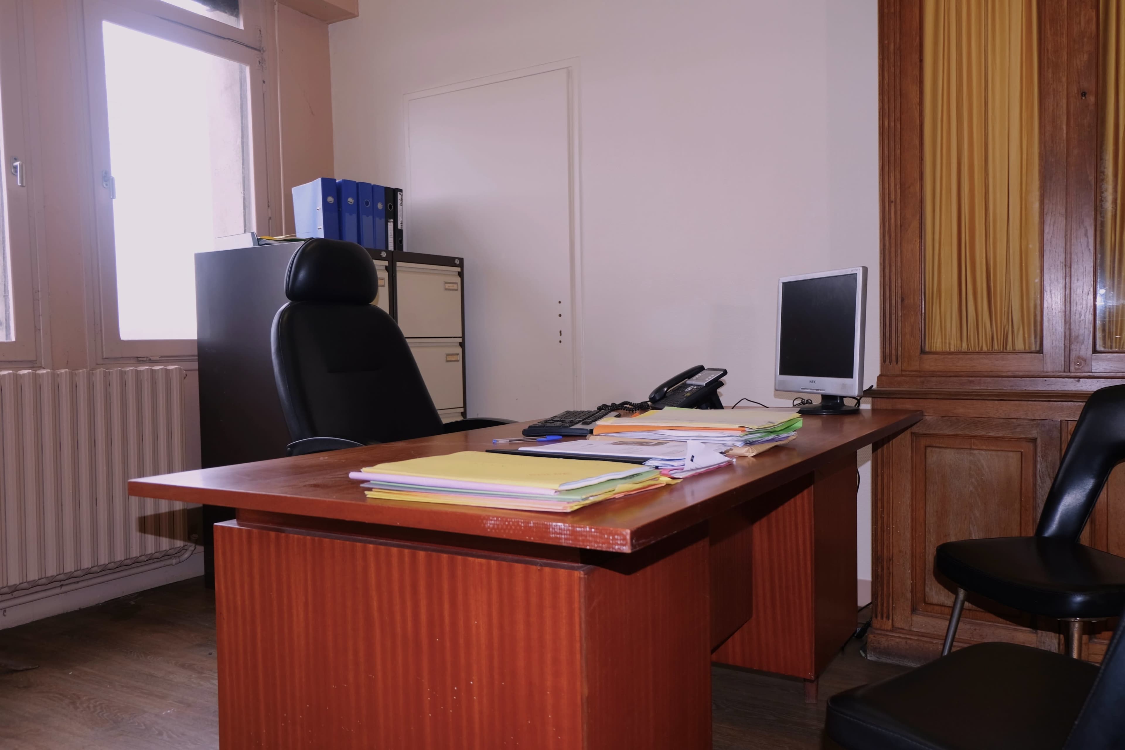 An office space with a desk, chair, computer, phone, filing cabinet, and documents arranged on the desk.