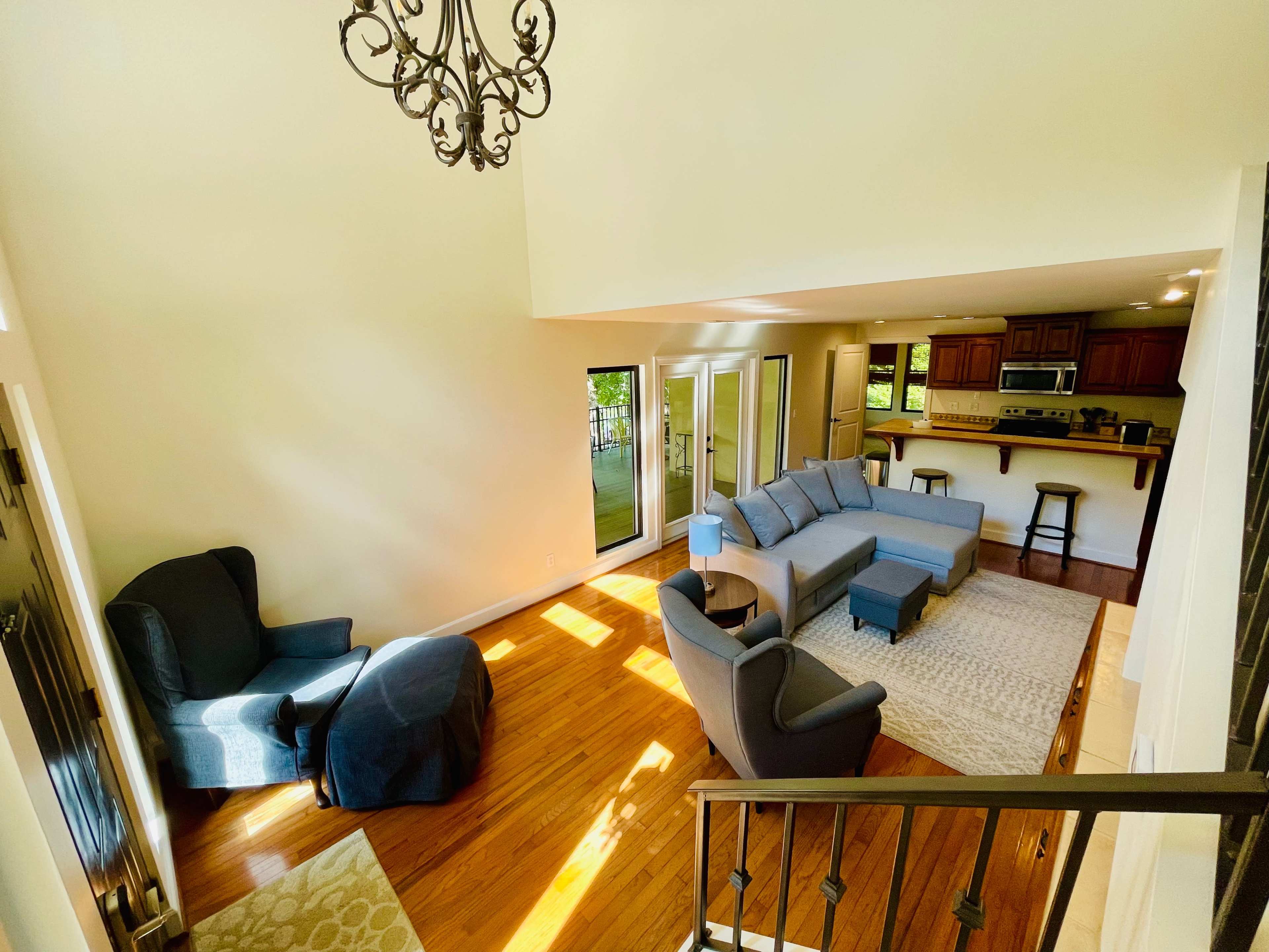 The image shows a spacious living room with hardwood floors, large windows, and a sectional sofa arranged around a coffee table.