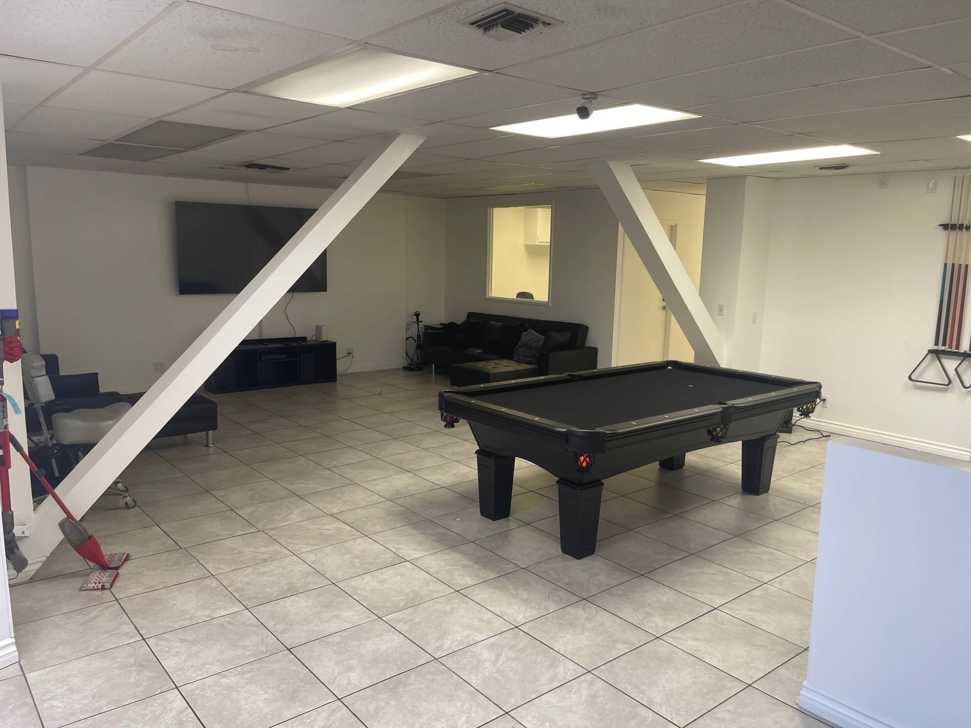 A spacious room with a pool table, a sectional sofa, a television mounted on the wall, and stark white walls.