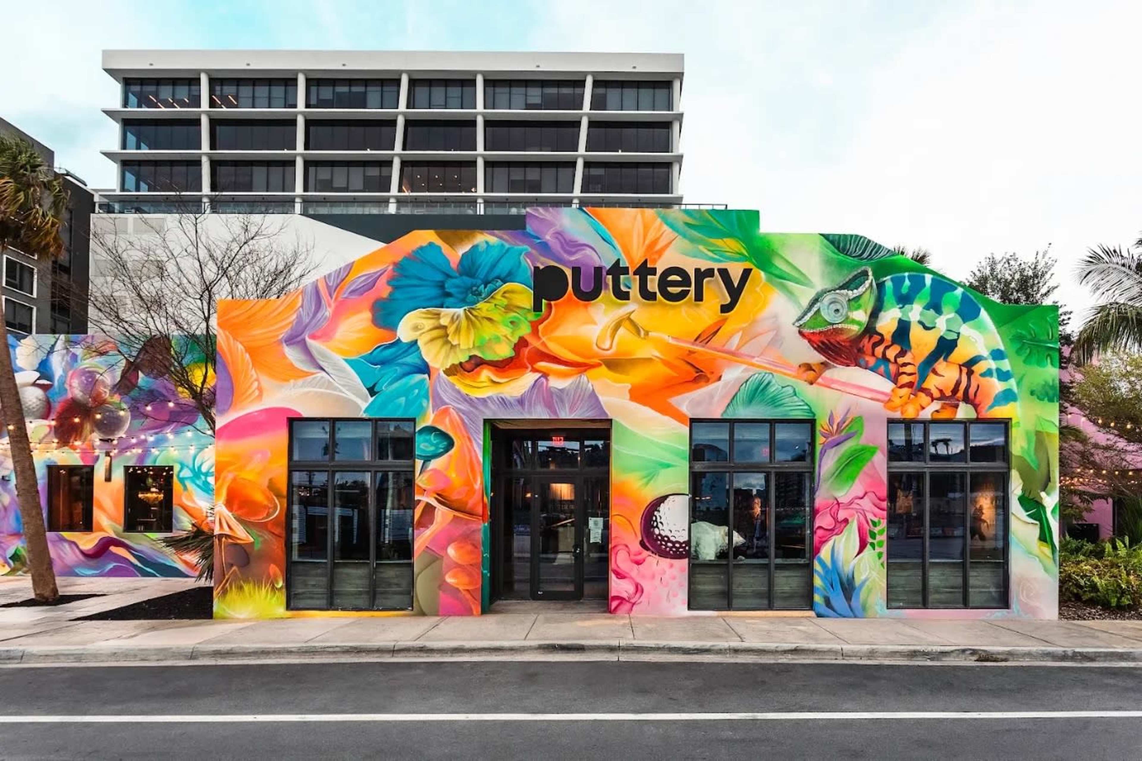The image shows a vibrant, mural-covered building with large windows, located on a street in a city setting.