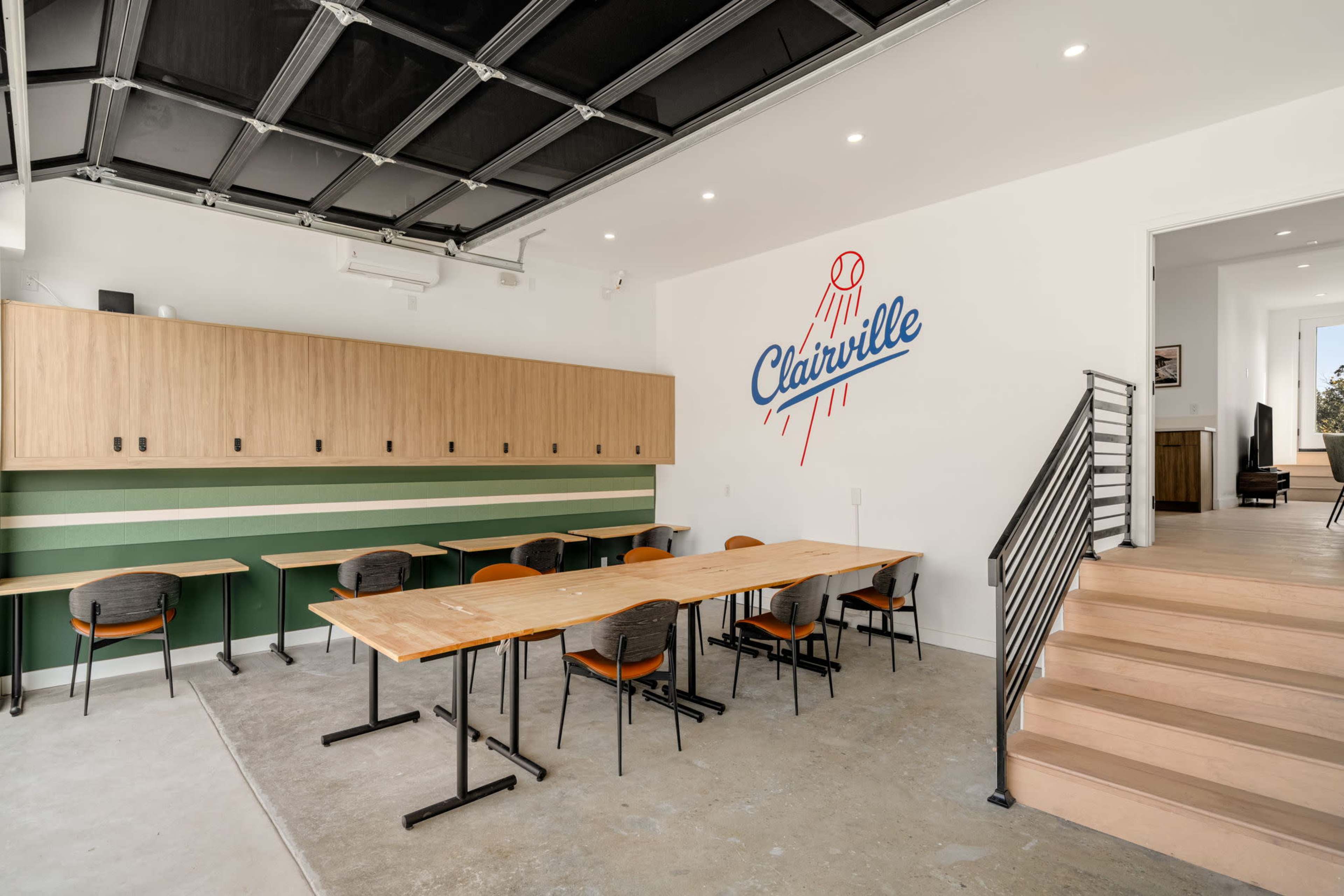 The image shows a modern classroom setting with wooden tables and chairs, a green accent wall, and a large wall-mounted sign featuring the name "Clairville."