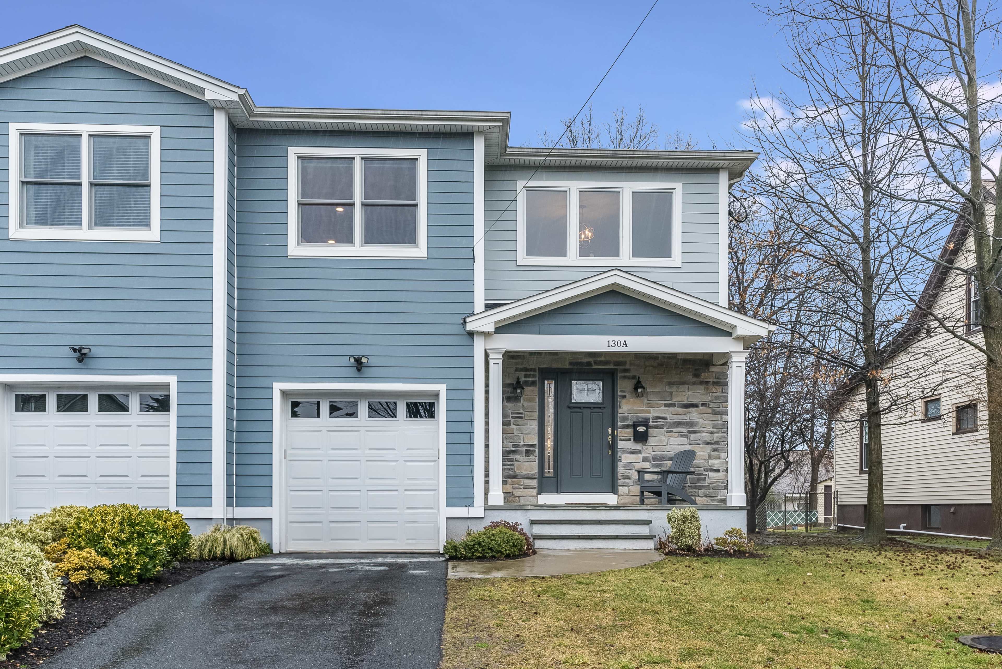 A blue, two-story townhouse with a stone-accented entrance, a driveway, and a garage on the left side.
